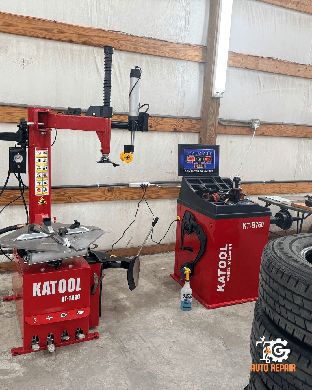 Workshop with tire repair equipment, including a red tire changer, a red tool cabinet, and a computer monitor on a red stand.