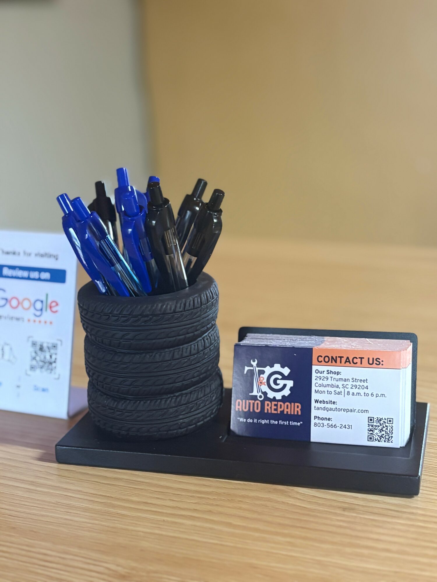 Pen holder made of stacked tires with blue and black pens, on a black tray with a business card and QR code.