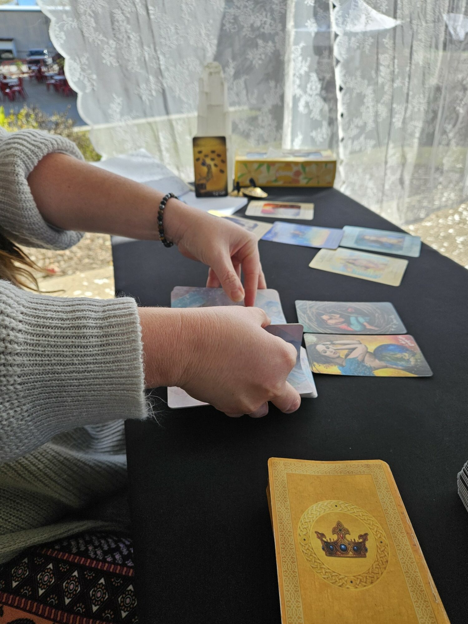 Child's hands arranging colorful cards on a black table, with a yellow card in the foreground and a window with curtains behind.