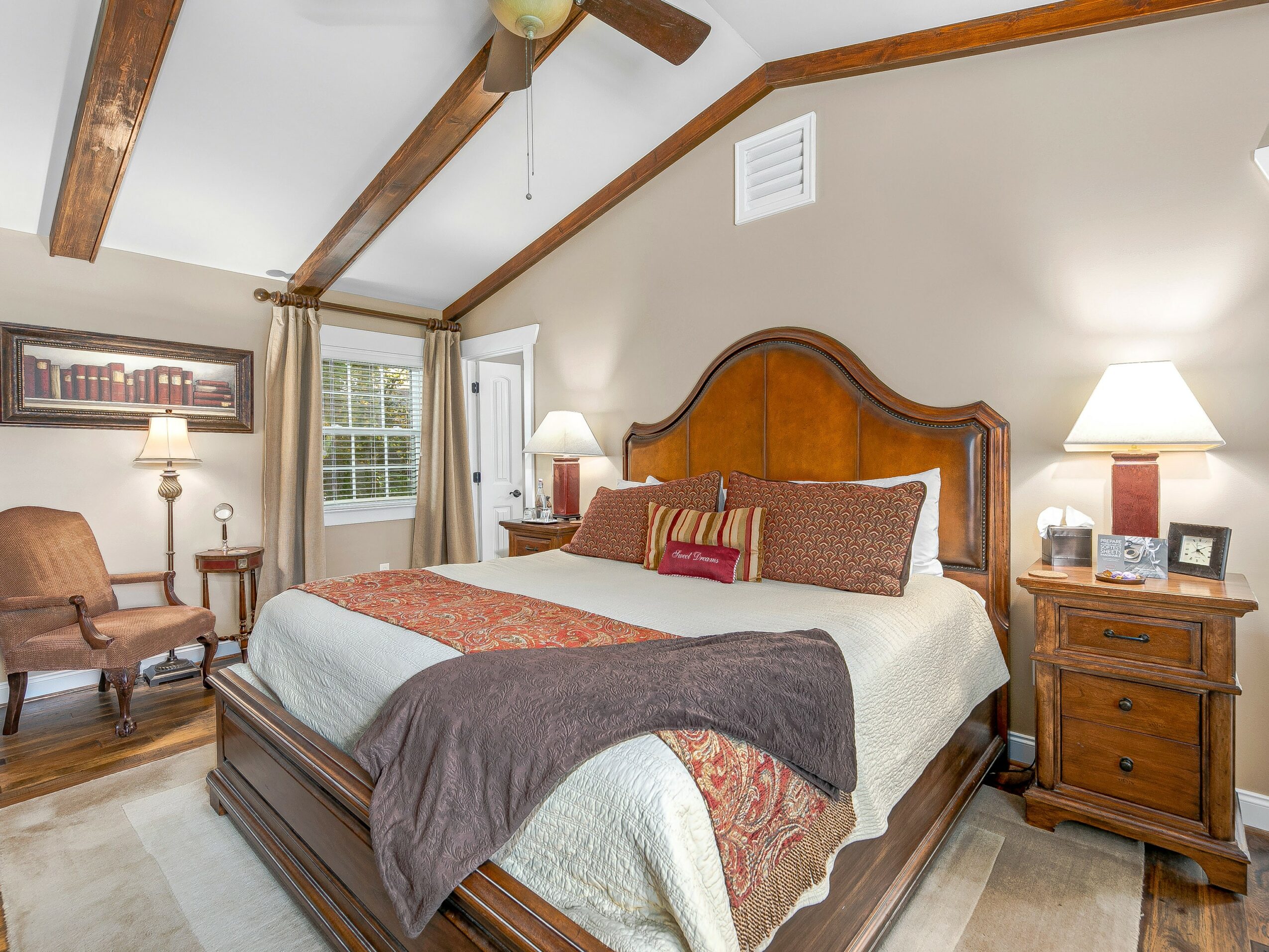 Bedroom with wooden bed, pillows, nightstands, lamps, window, and armchair.