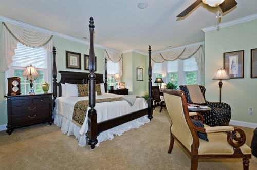 Bedroom with four-poster bed, nightstands, lamps, armchair, and windows with curtains.