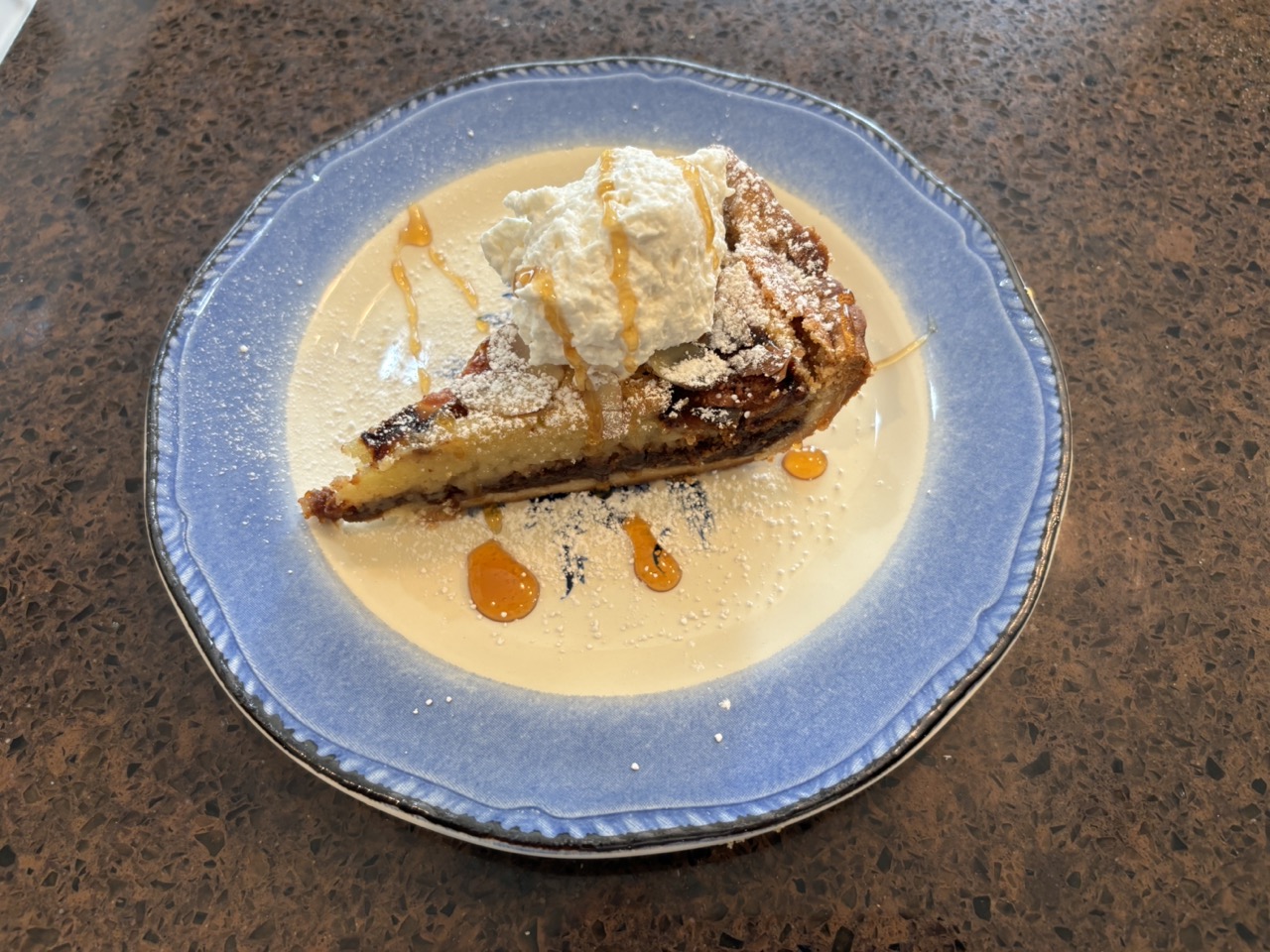 Slice of pie with ice cream and caramel sauce on a blue plate, on a brown surface.