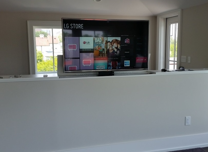 Large flat-screen TV on a white wall, with windows on both sides showing outdoor scenery.