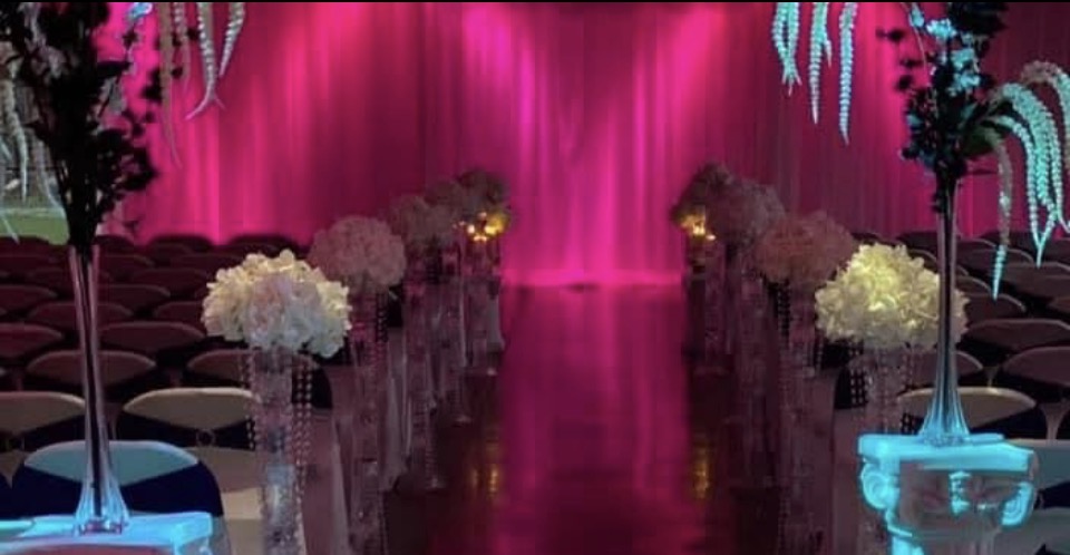Event space with pink backdrop, floral arrangements, and seating, decorated for a celebration or ceremony.