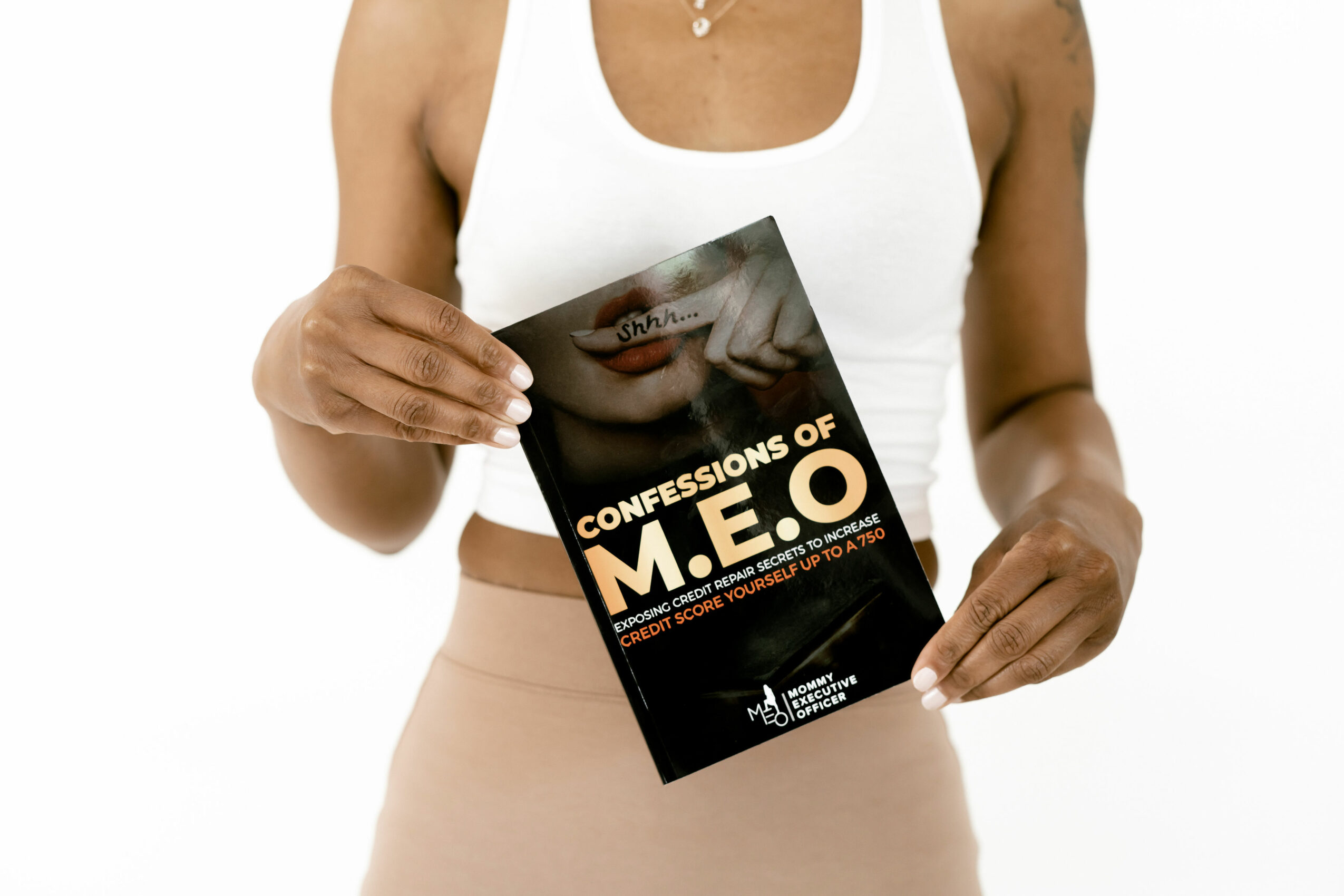 Person holding a book titled 'Confessions of M.E.O' with a partial face image on the cover, wearing a white top and beige pants.