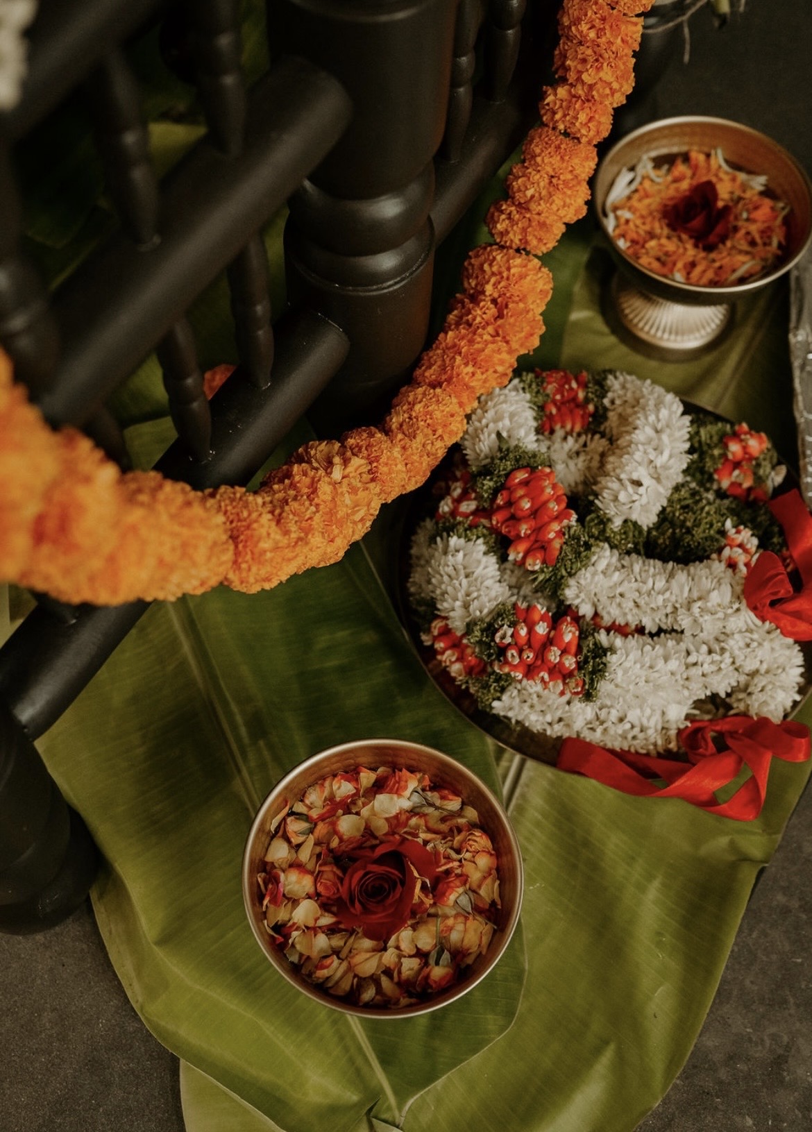 Decorative flower garland, bowls with flowers and petals, and a floral arrangement on a green cloth surface.