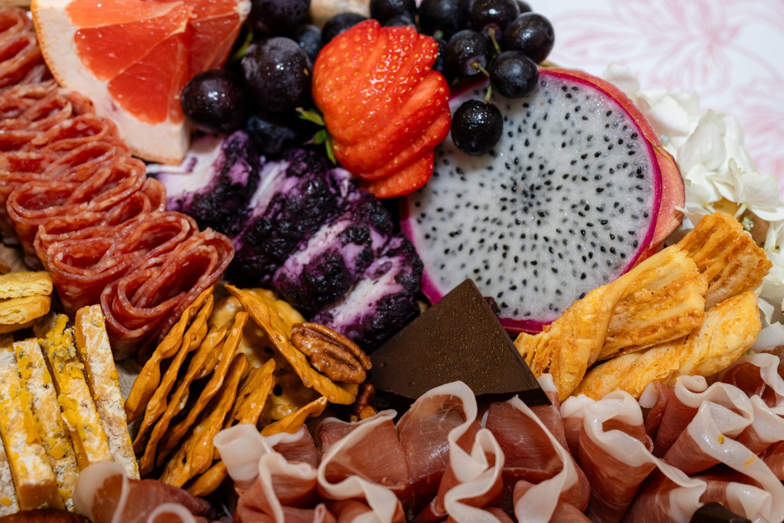 Assorted sliced fruits and berries on a pink patterned surface, including dragon fruit, strawberry, blueberries, and grapefruit slices.