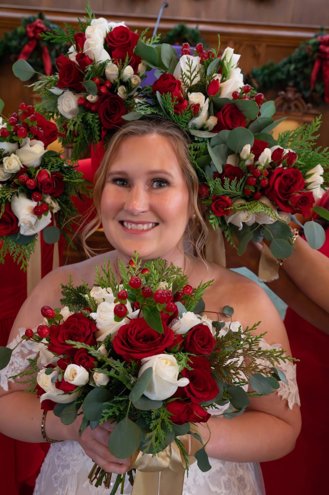 Young woman holding a bouquet of red and white flowers, smiling, with a large floral arrangement behind her.