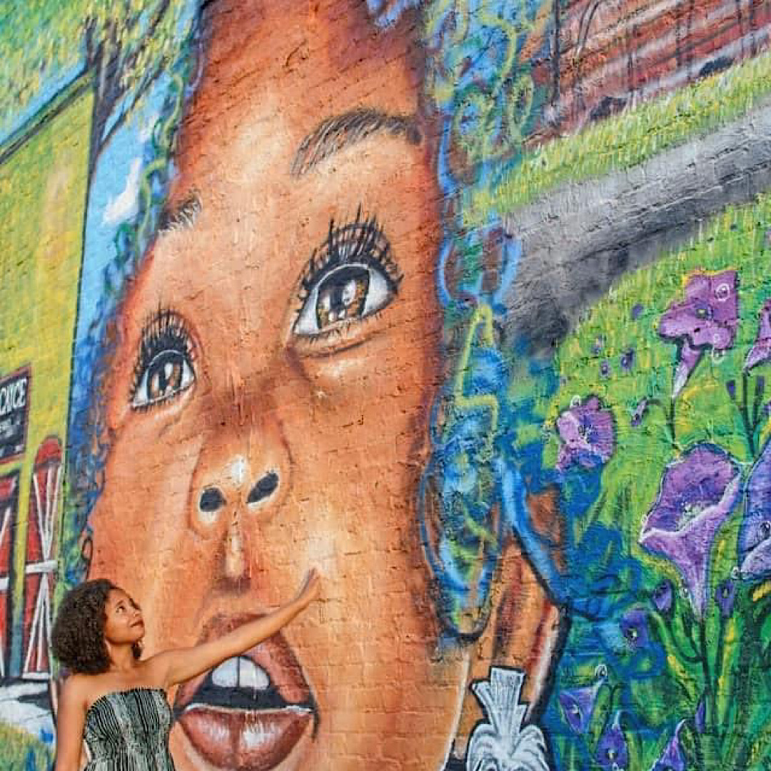 Close-up of a mural featuring a woman's face with detailed eyes and lips, surrounded by colorful flowers and graffiti.