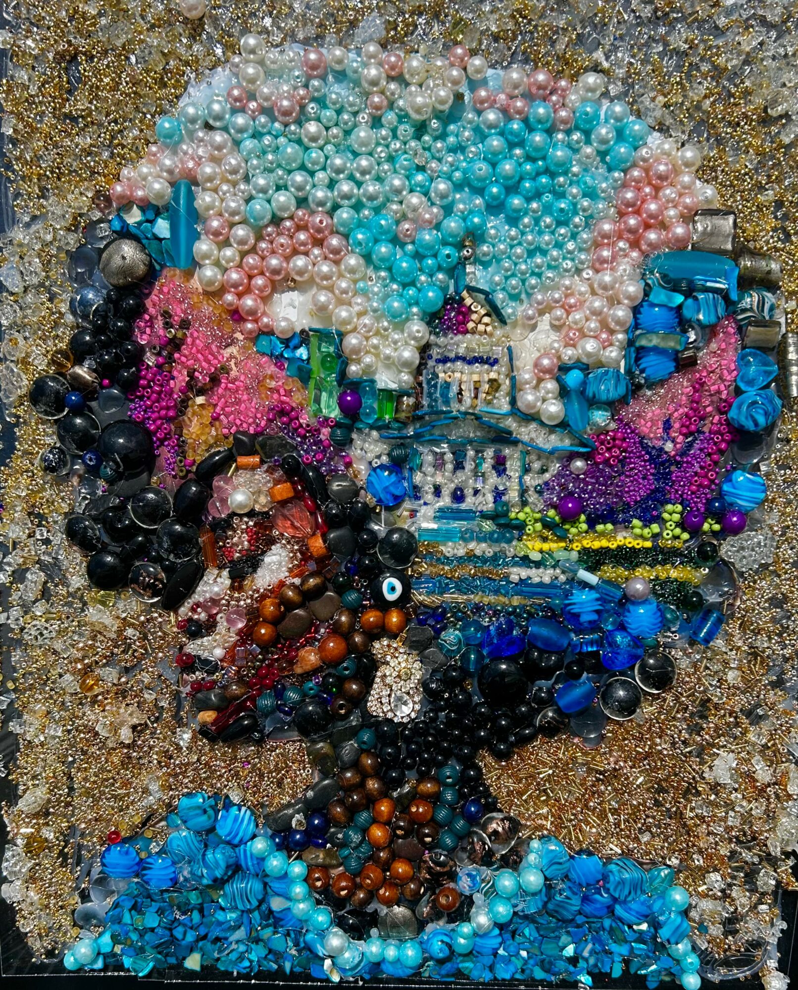 Portrait of a woman made from colorful beads and small objects on a sandy background.