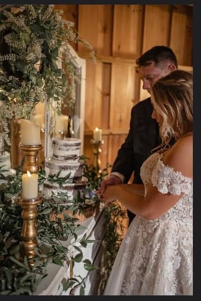 Bride and groom standing at a decorated table with candles and greenery, inside a wooden venue.