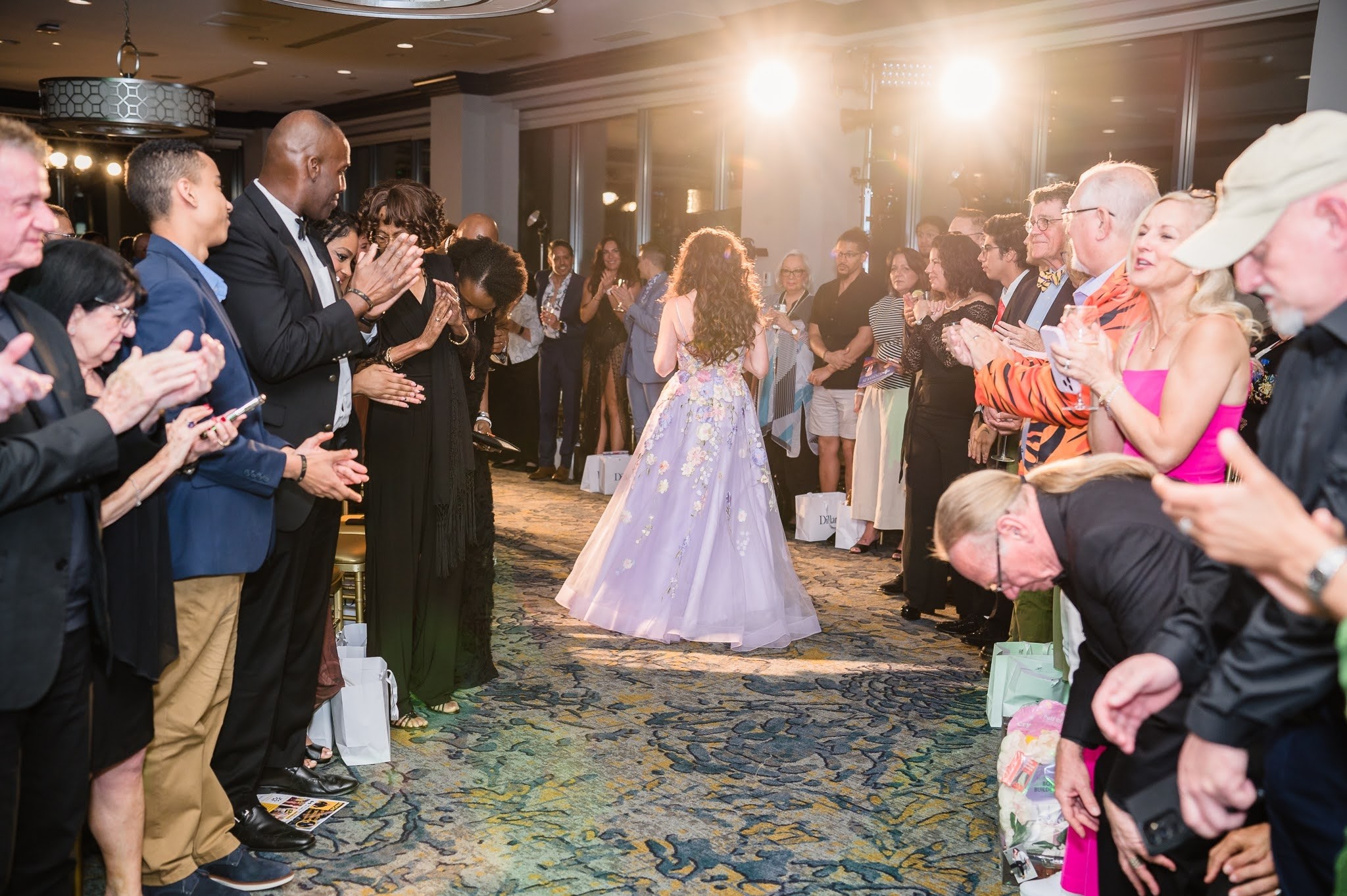 People form a circle clapping around a girl in a light-colored dress dancing in a decorated indoor venue.