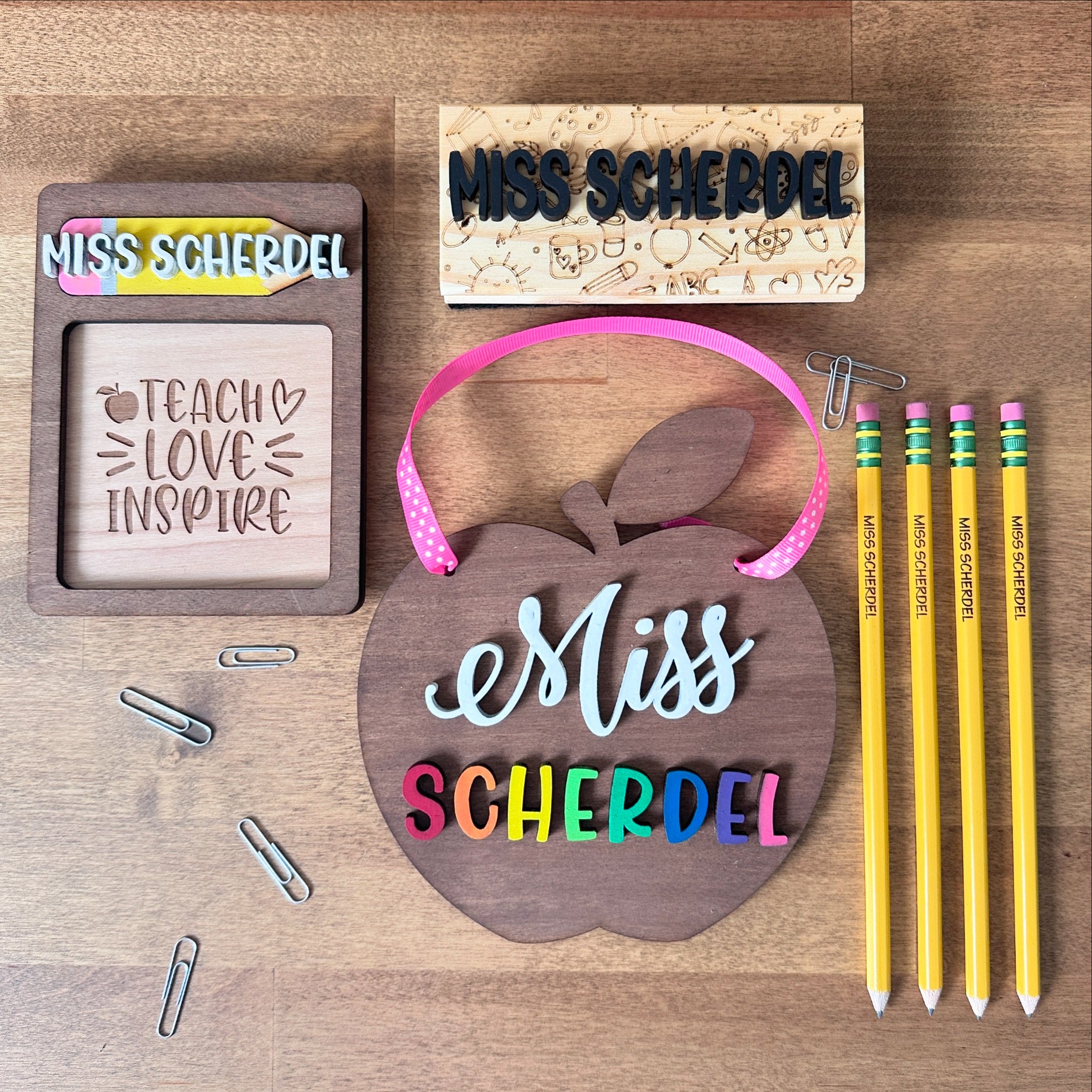 School supplies including a name tag, paper cutout, headband, colorful pens, and paper clips on a wooden surface.