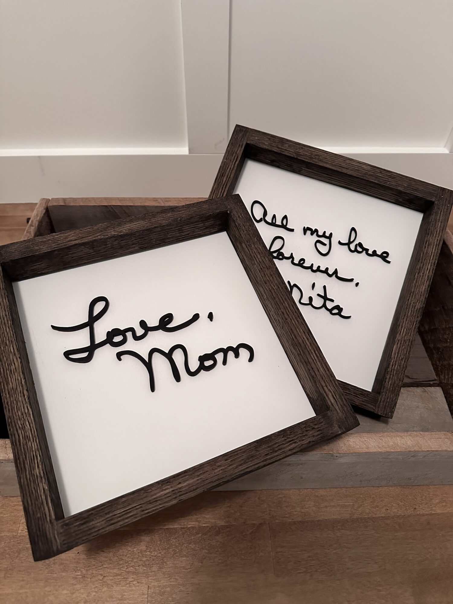 Two framed signs with handwritten messages, one reading 'love, Mom' and the other partially visible, placed on a wooden surface.