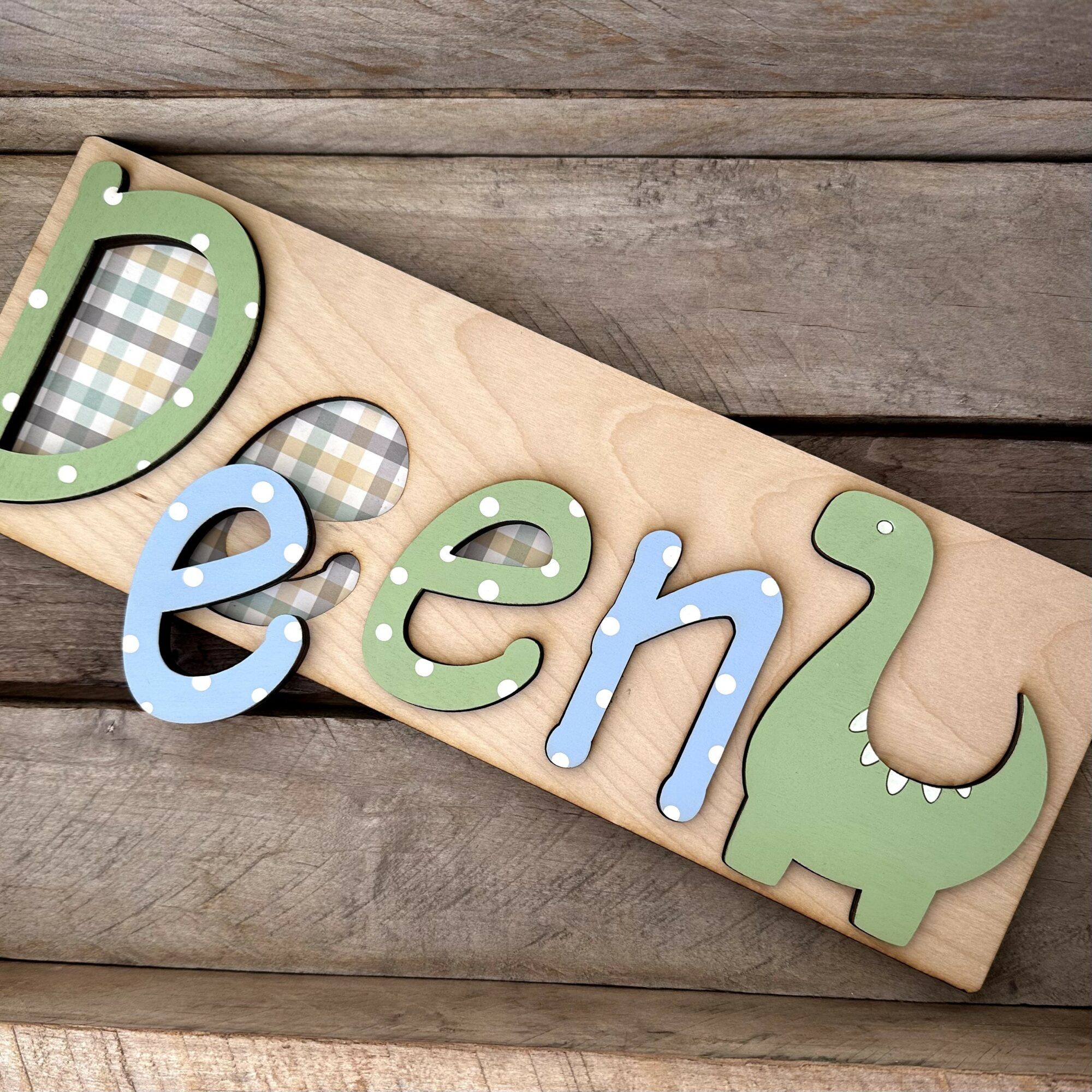 Colorful foam letters spelling 'D' and 'e' on a wooden board, with a green dinosaur shape, on a wooden surface.