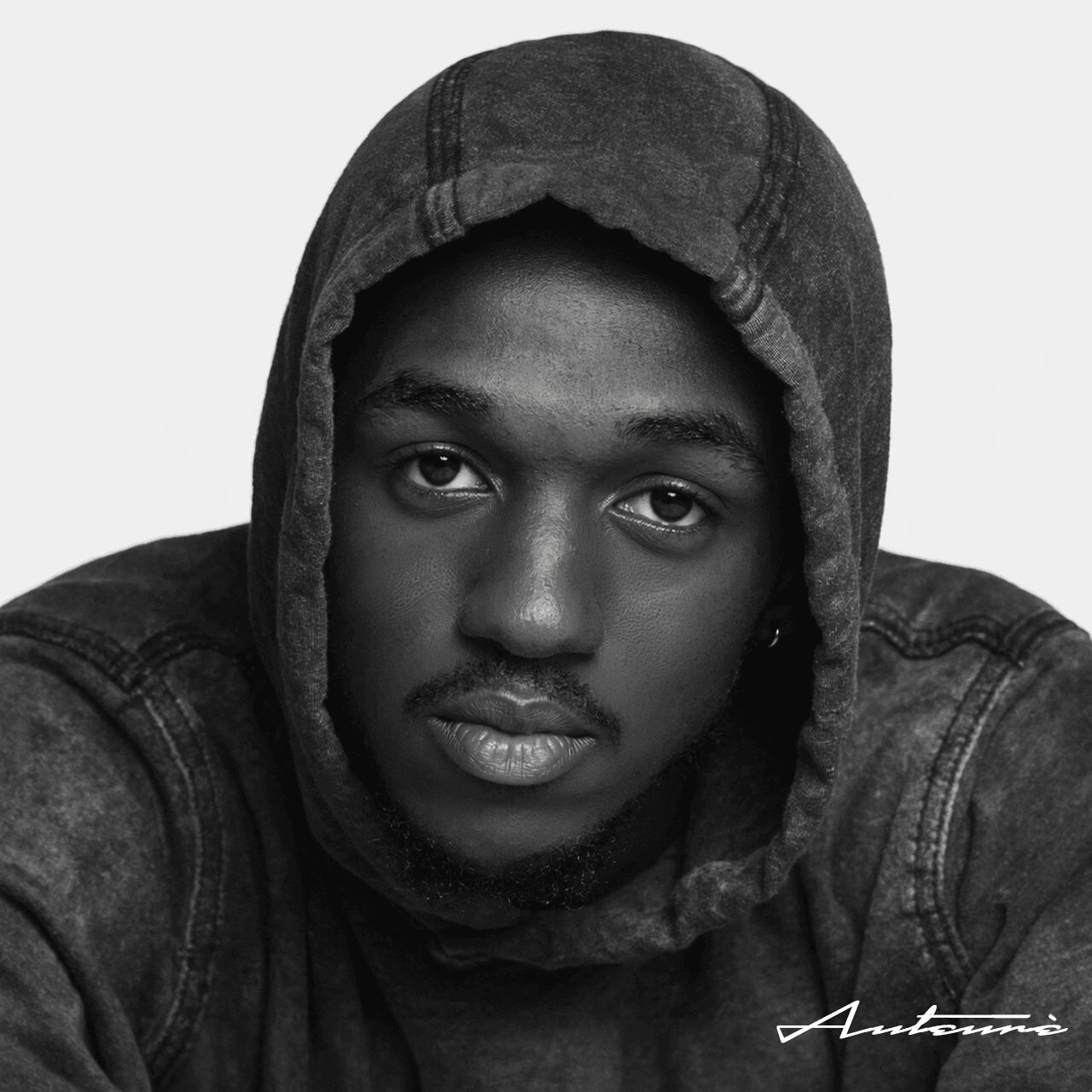 Young person wearing a hooded jacket, looking directly at the camera, with a neutral expression, in black and white.