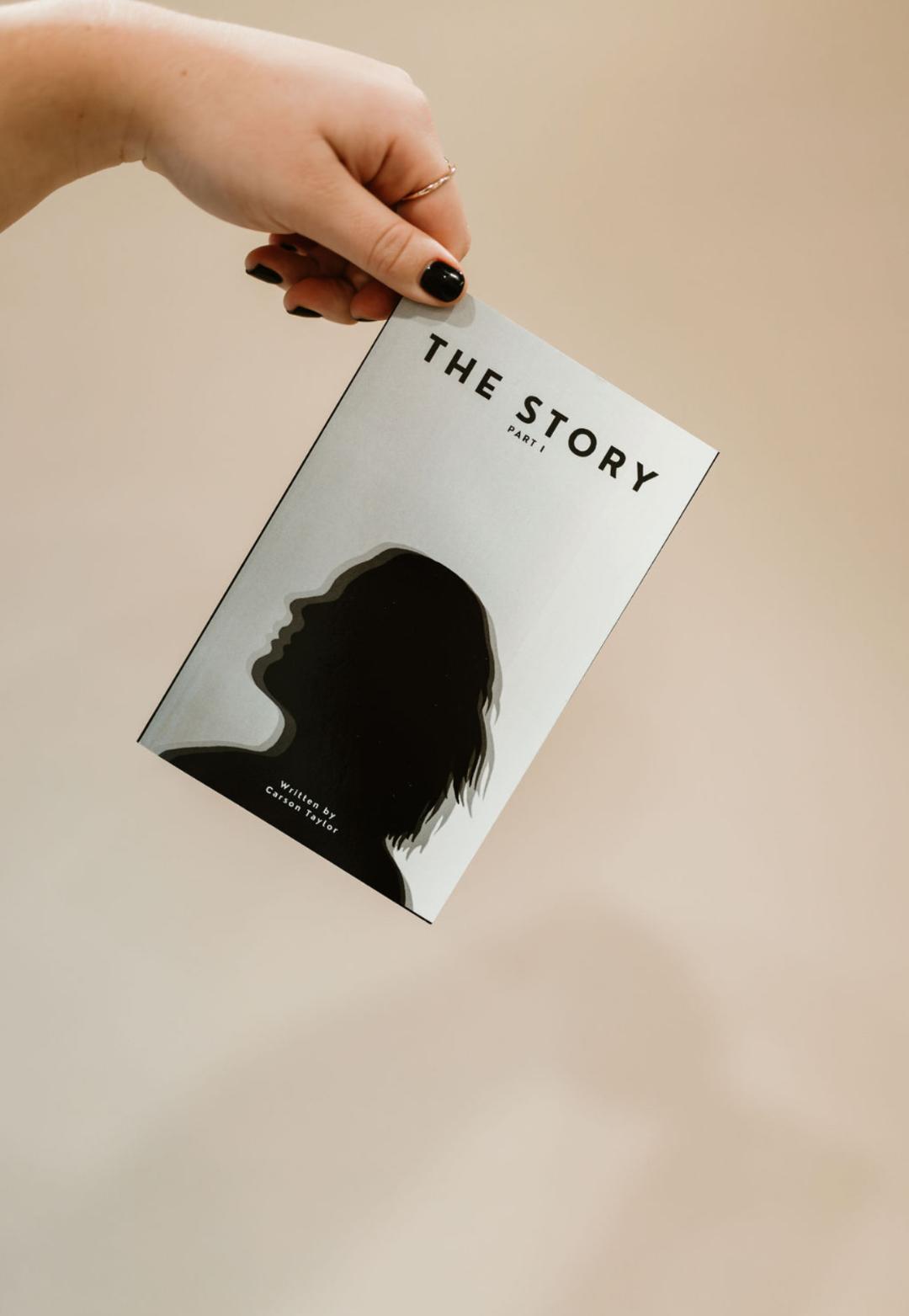 Hand holding a book titled 'The Story' with a silhouette of a person's profile on the cover.