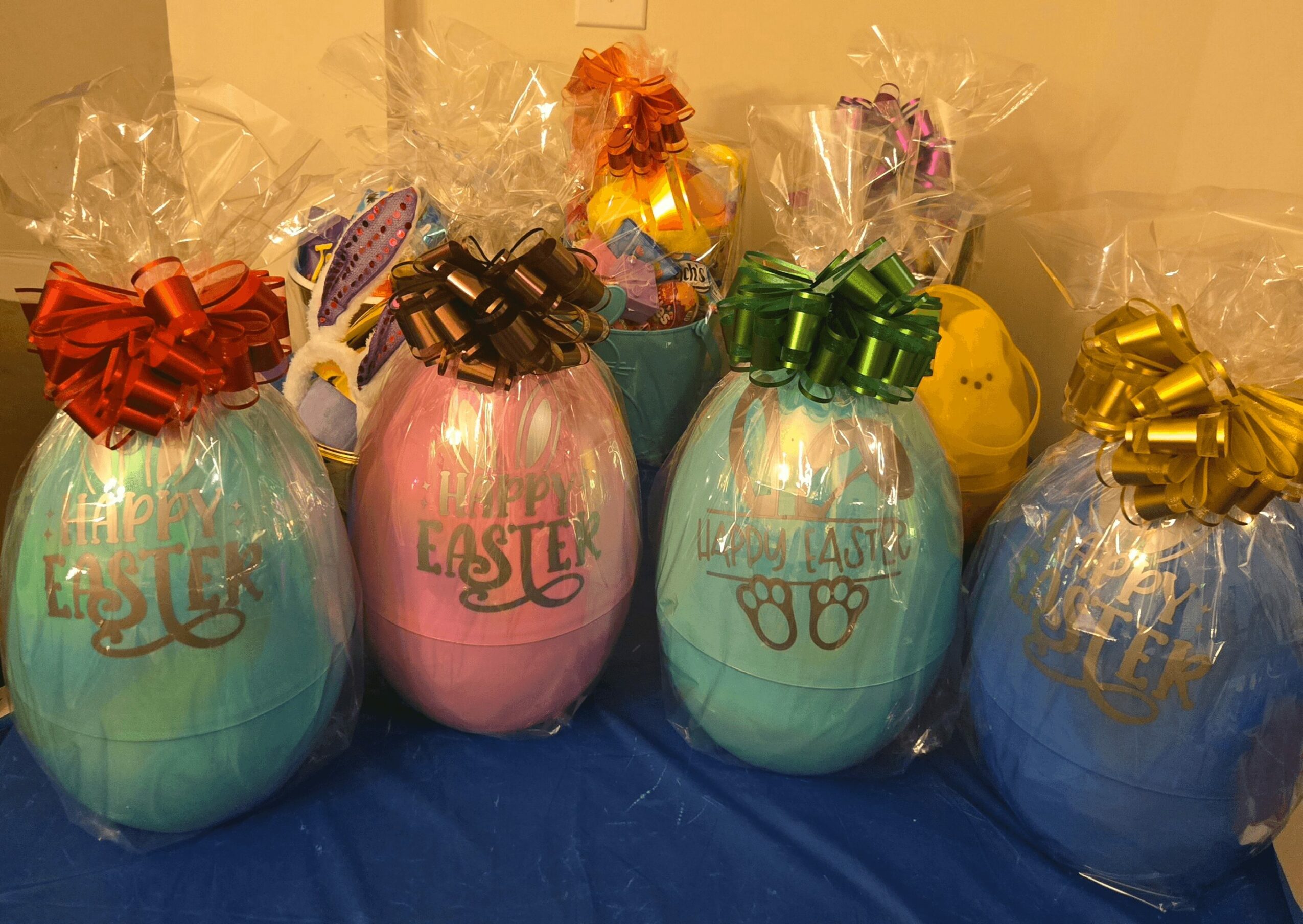 Four pastel-colored Easter eggs wrapped in clear plastic with large decorative bows on top, arranged on a blue surface.