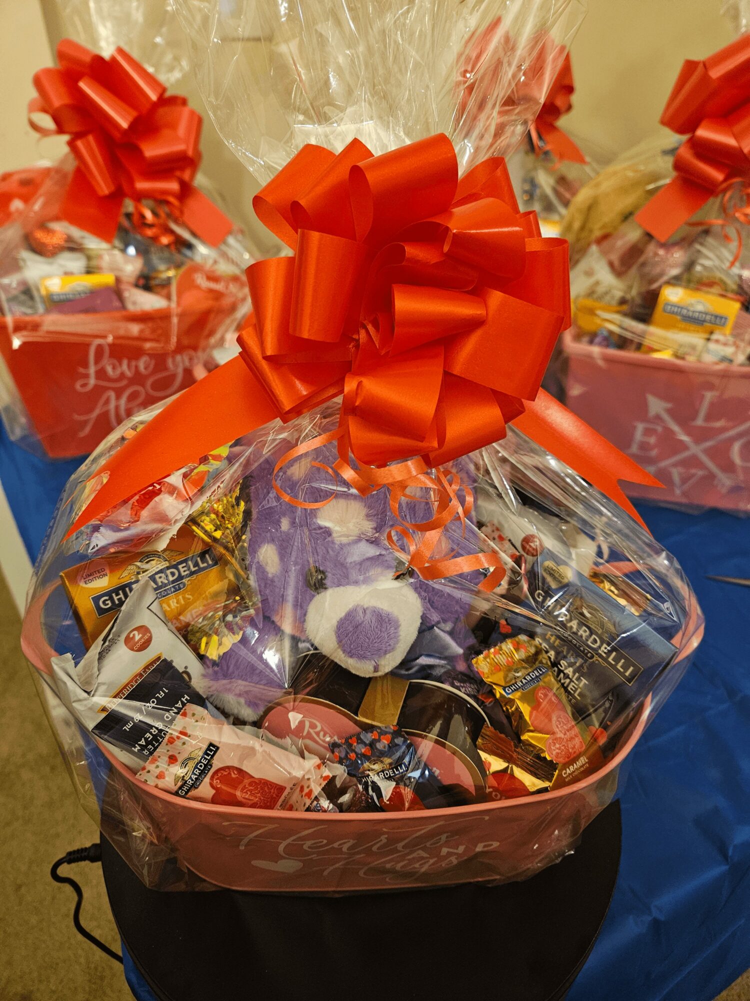 Gift basket wrapped in clear plastic with an orange bow, containing snacks and small items.