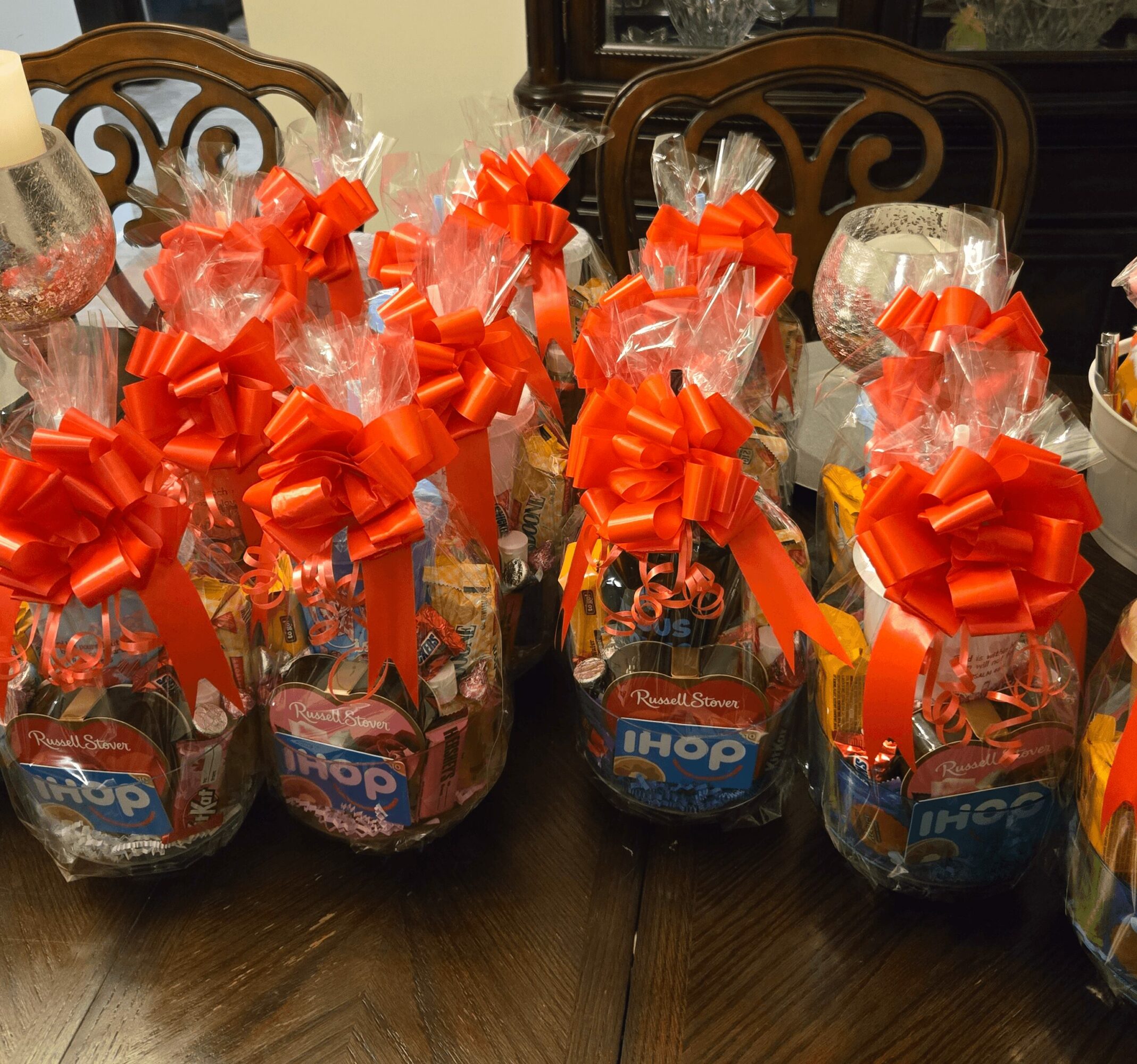 Multiple gift baskets wrapped in clear plastic with large red bows, placed on a wooden table.