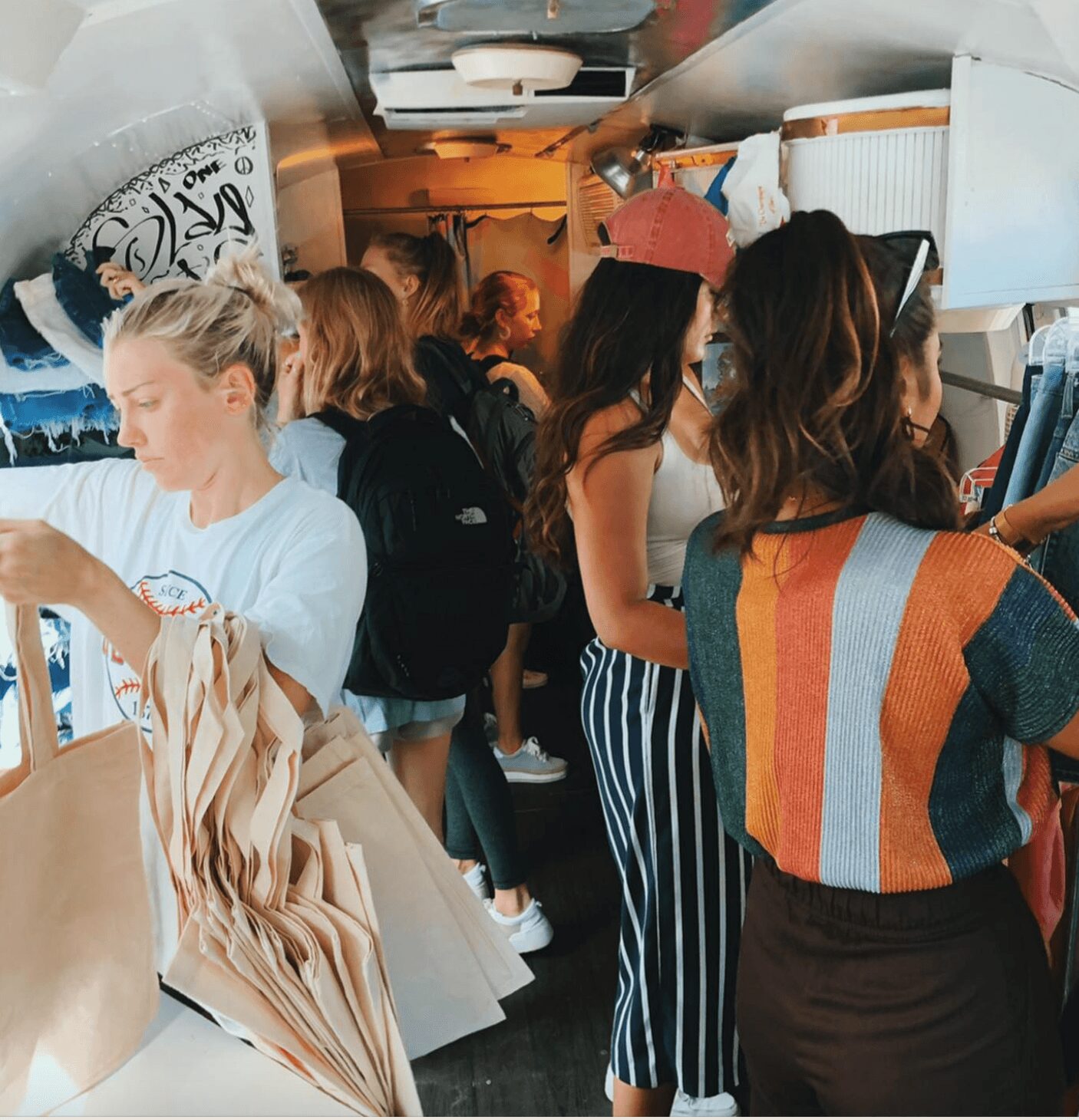 Group of people inside a small store, some browsing and others talking, with shelves and items around.
