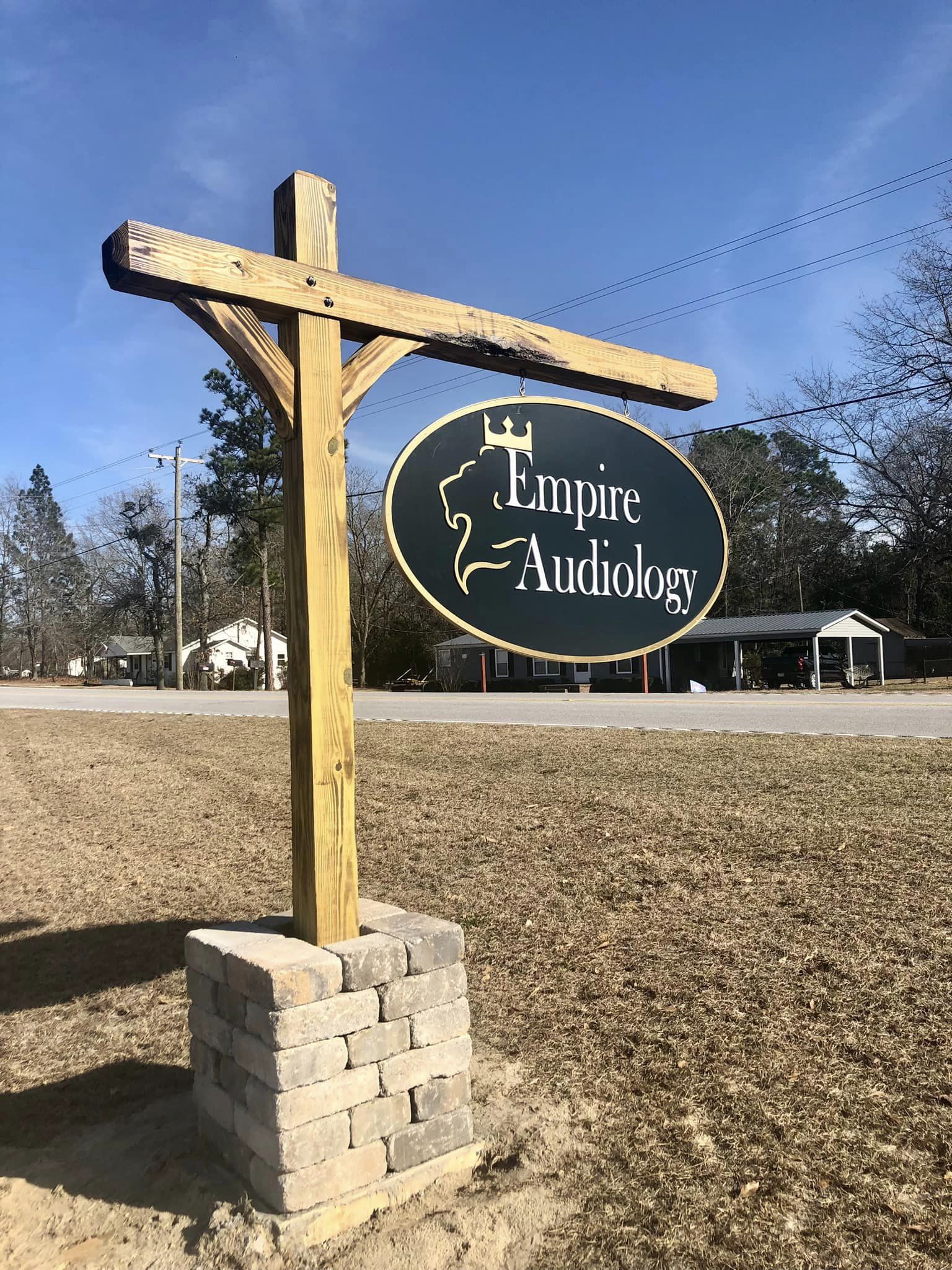 Wooden signpost with an oval sign reading 'Empire Audiology' on a grassy area, with trees and buildings in the background.