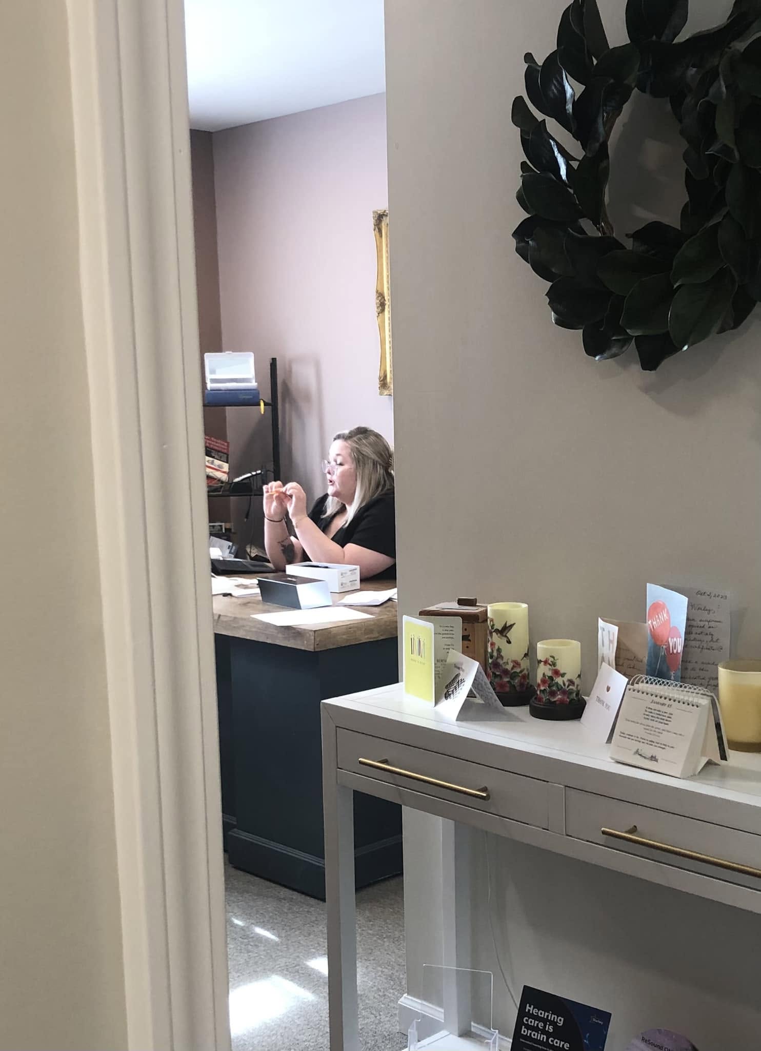 Person sitting at a desk working on a computer, with a wall and decorative wreath nearby.