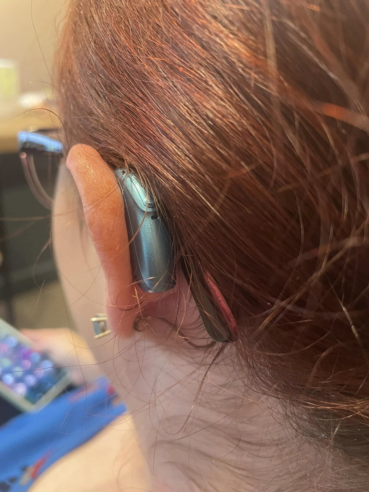 Person with red hair wearing a blue headset, holding a remote control, in a room with blurred background.