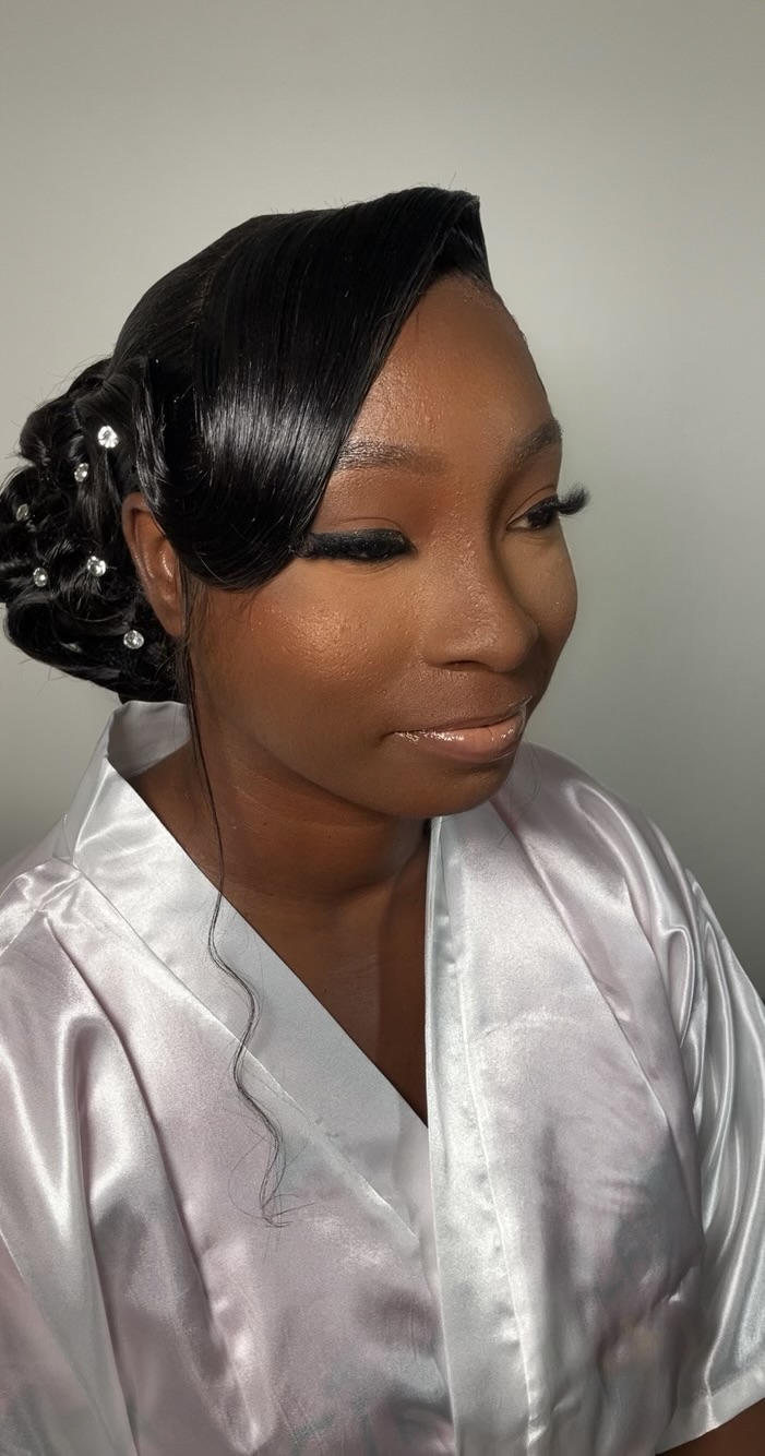 Woman with styled black hair and makeup, wearing a shiny silver satin robe, looking to the side.
