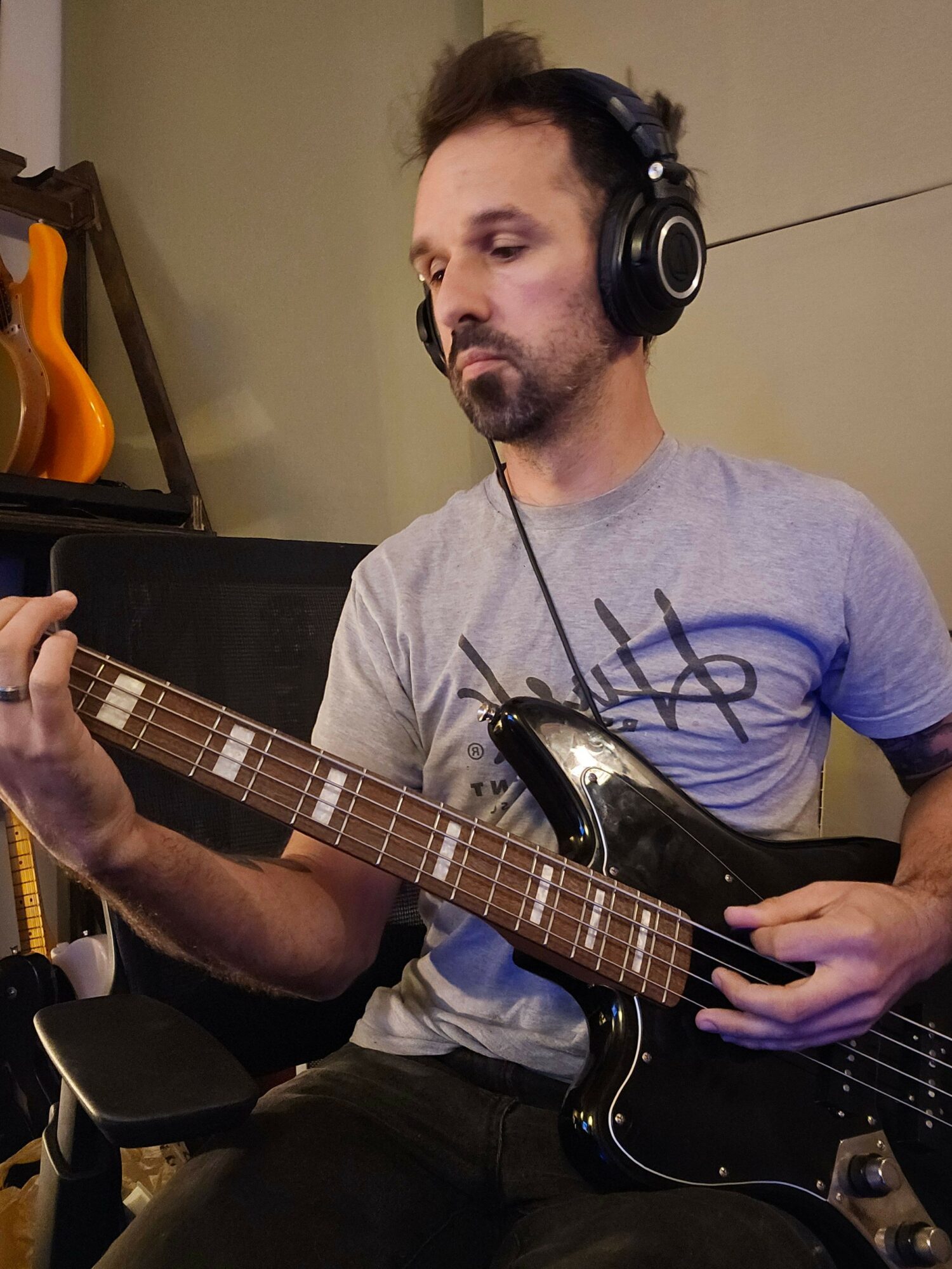 Person wearing headphones playing an electric guitar, sitting at a desk with a computer mouse and keyboard.