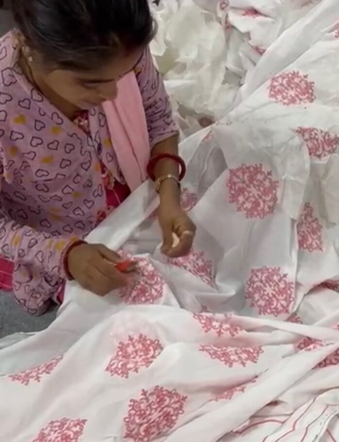 Child holding scissors and cutting white fabric with pink floral patterns, focused on the task.