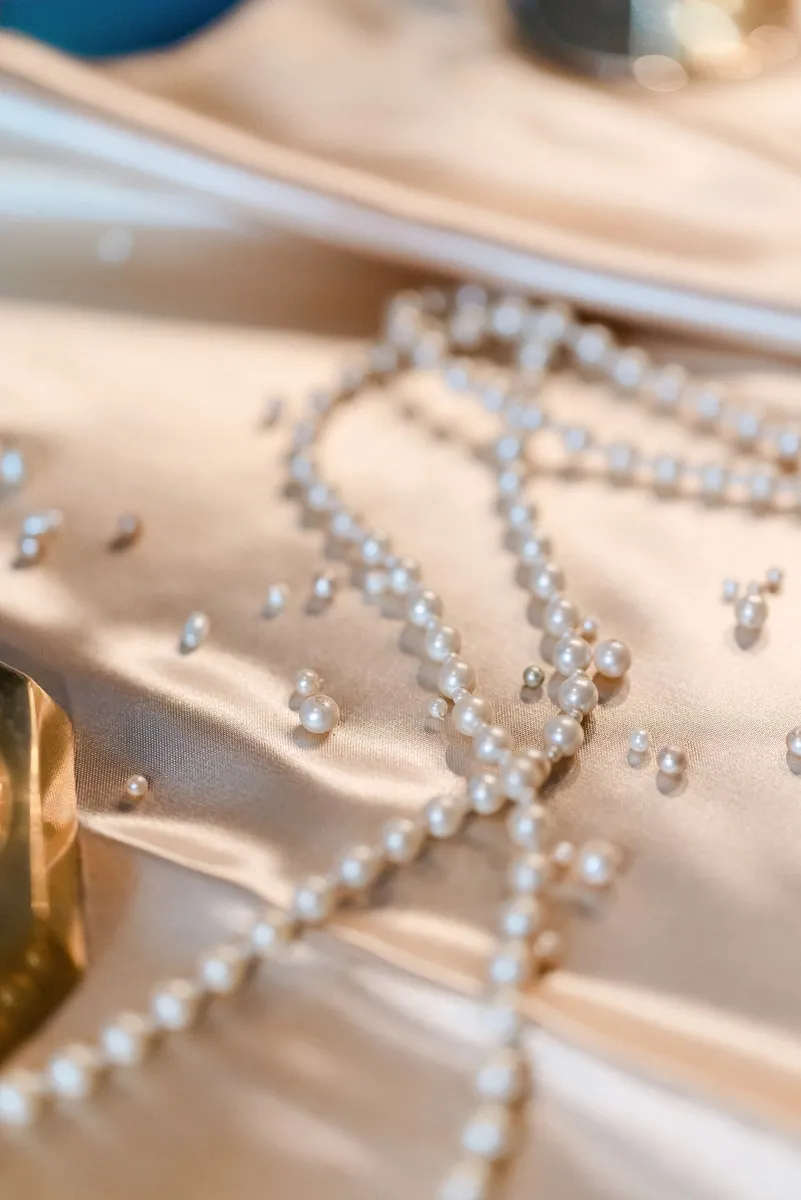 Pearl necklaces and scattered pearls on silky fabric with a blurred background.
