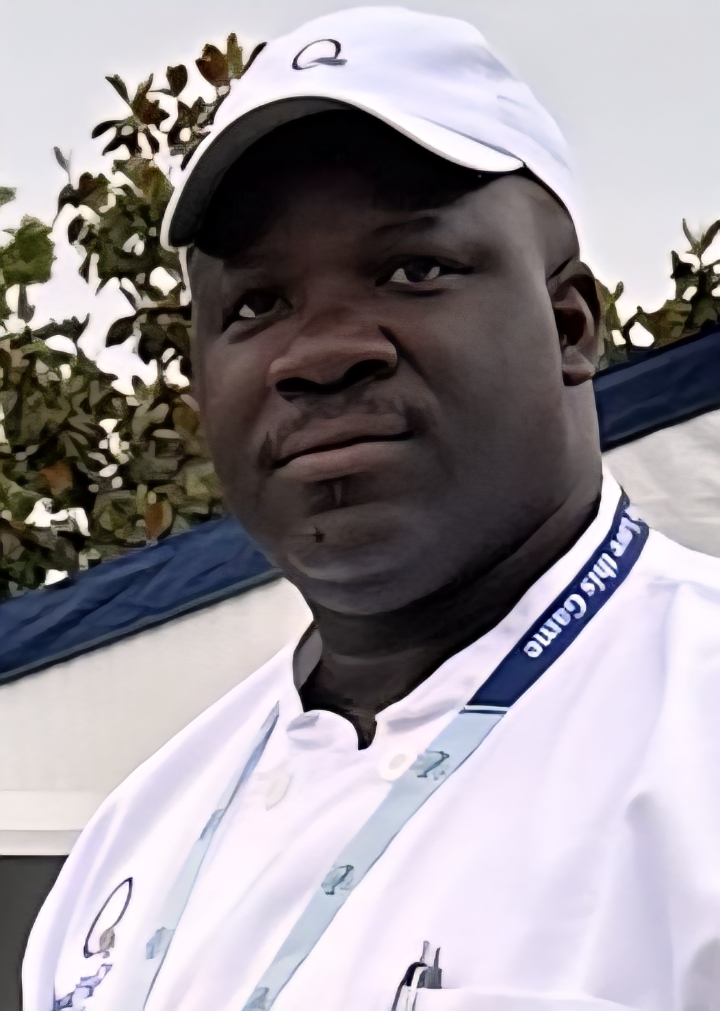 Man wearing white cap and shirt, outdoors with trees in background.