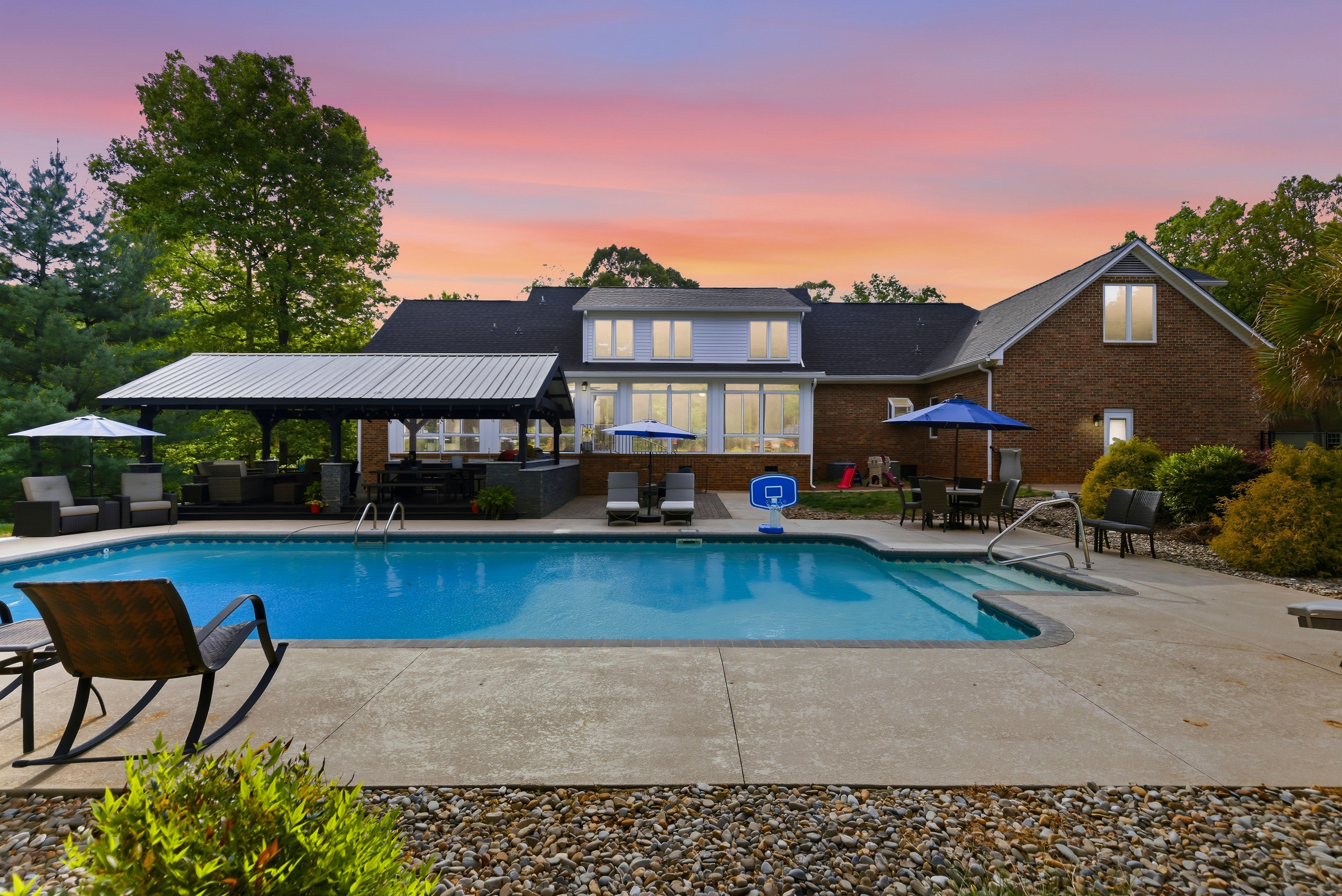 Swimming pool with lounge chairs, umbrellas, and a building with large windows at sunset.