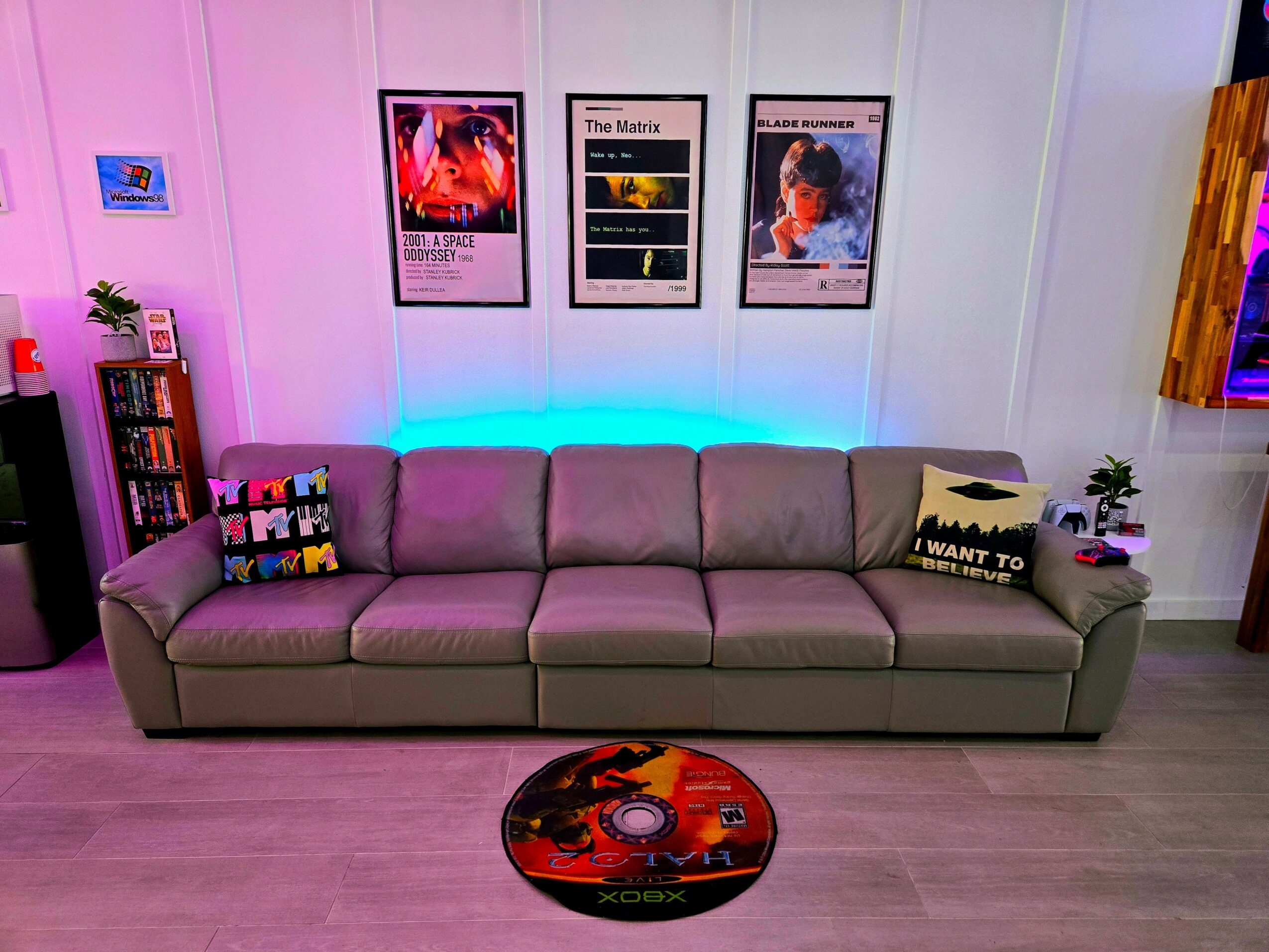 Long gray sofa with colorful pillows in a room with framed posters on the wall and a small round rug in front.