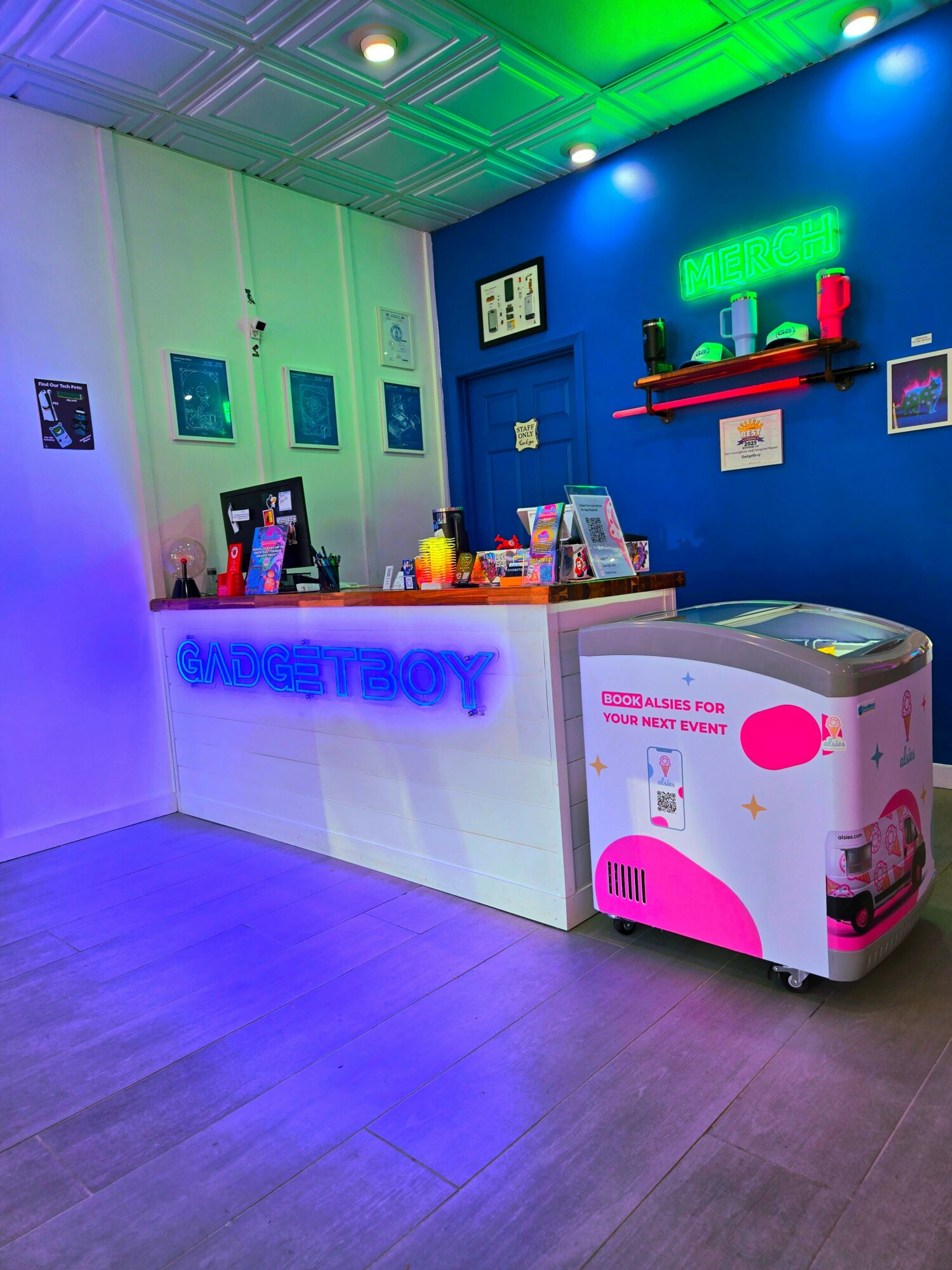 Ice cream shop counter with neon signs, colorful decorations, and an ice cream freezer, illuminated by vibrant lighting.
