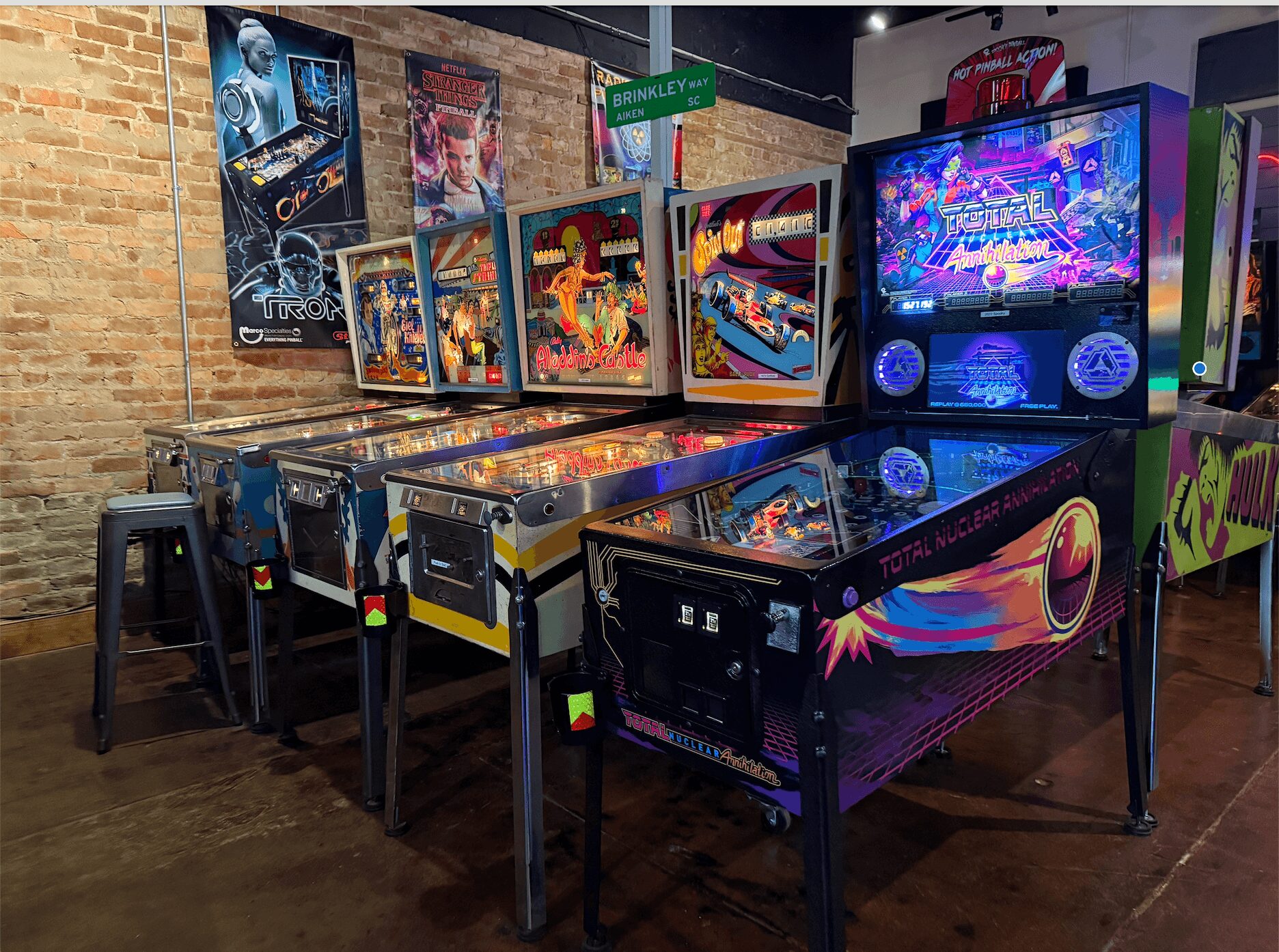 Pinball machines and arcade games in a room with brick walls and wooden floors.