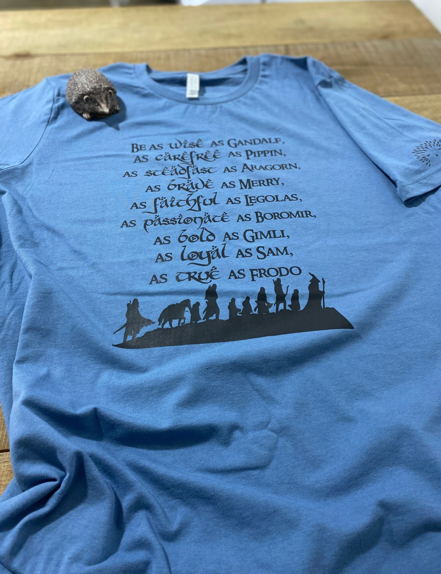 Blue T-shirt with a black silhouette of people walking, and text in a foreign language above it.