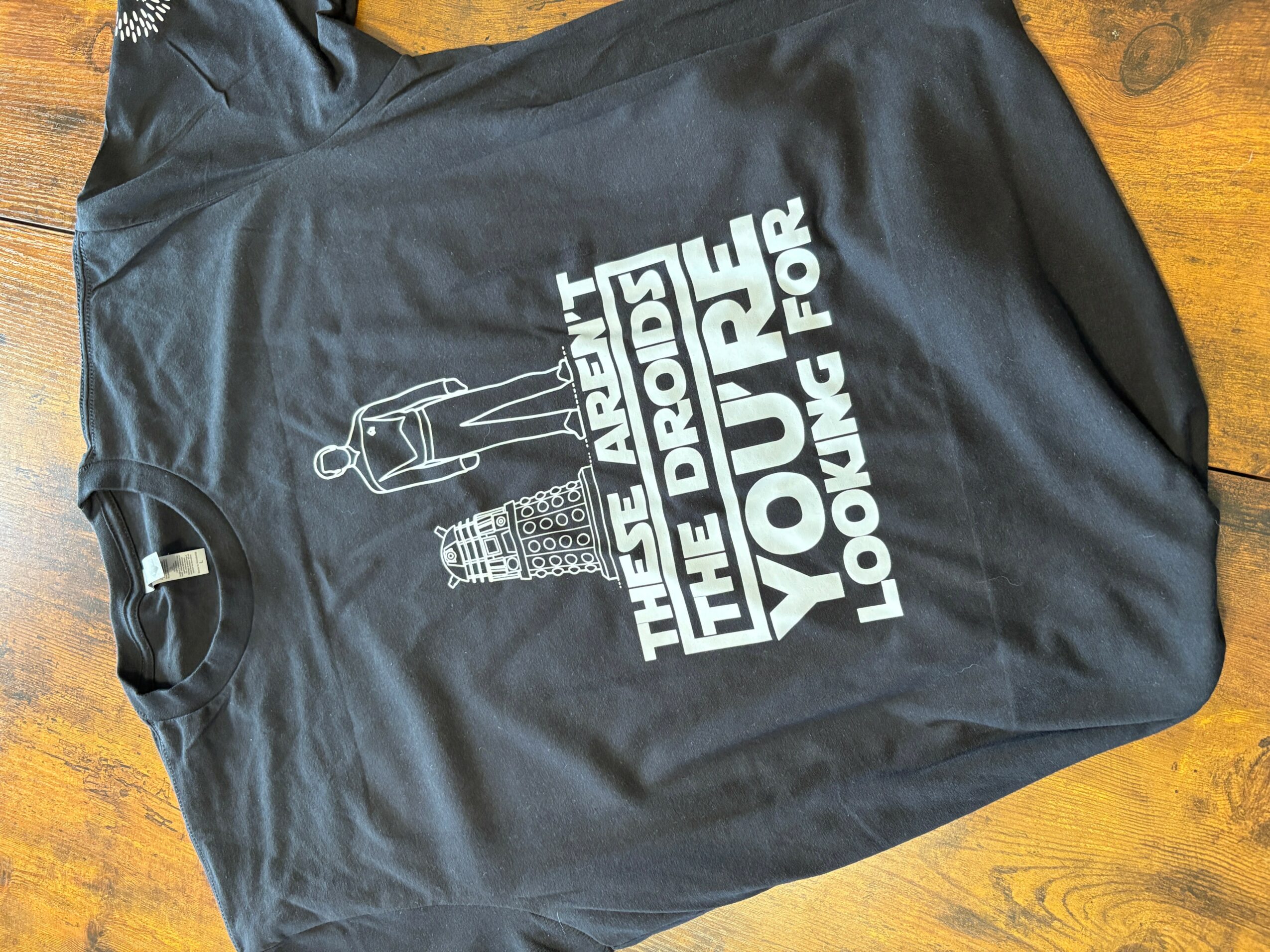 Black T-shirt with white text and graphics, featuring a person and buildings, and the phrase 'The above the airport, the drone for your looking for'.