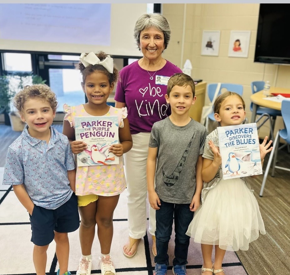 A woman with four children in a classroom, holding books about penguins and blues, smiling at the camera.