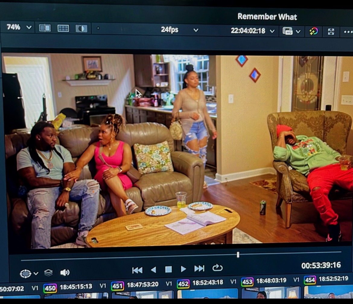 Living room with four people, two sitting on a sofa, one standing, and one lying on an armchair, with a coffee table and decorations.