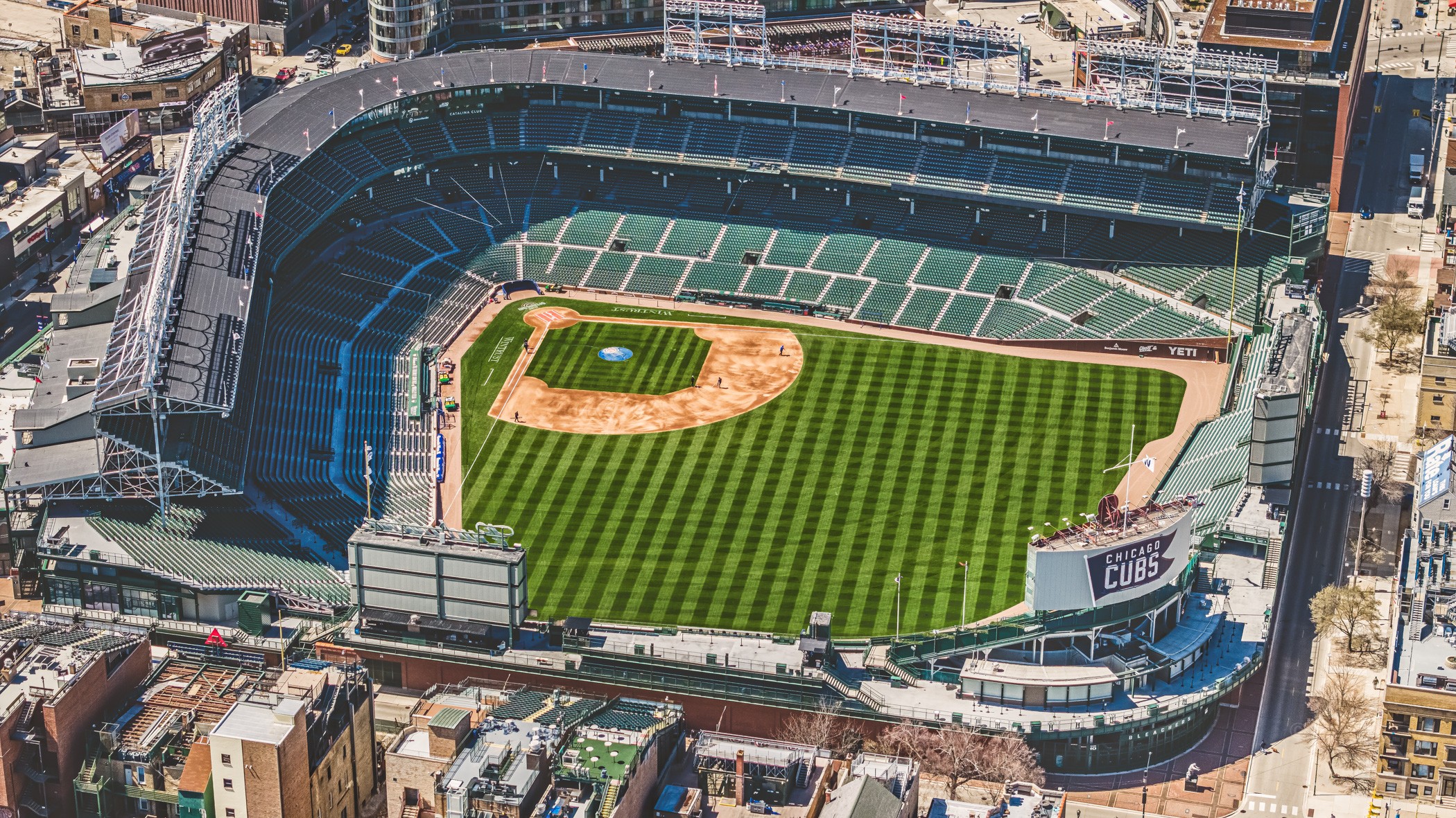 Aerial view of a baseball stadium with green field and seating areas, surrounded by city buildings.