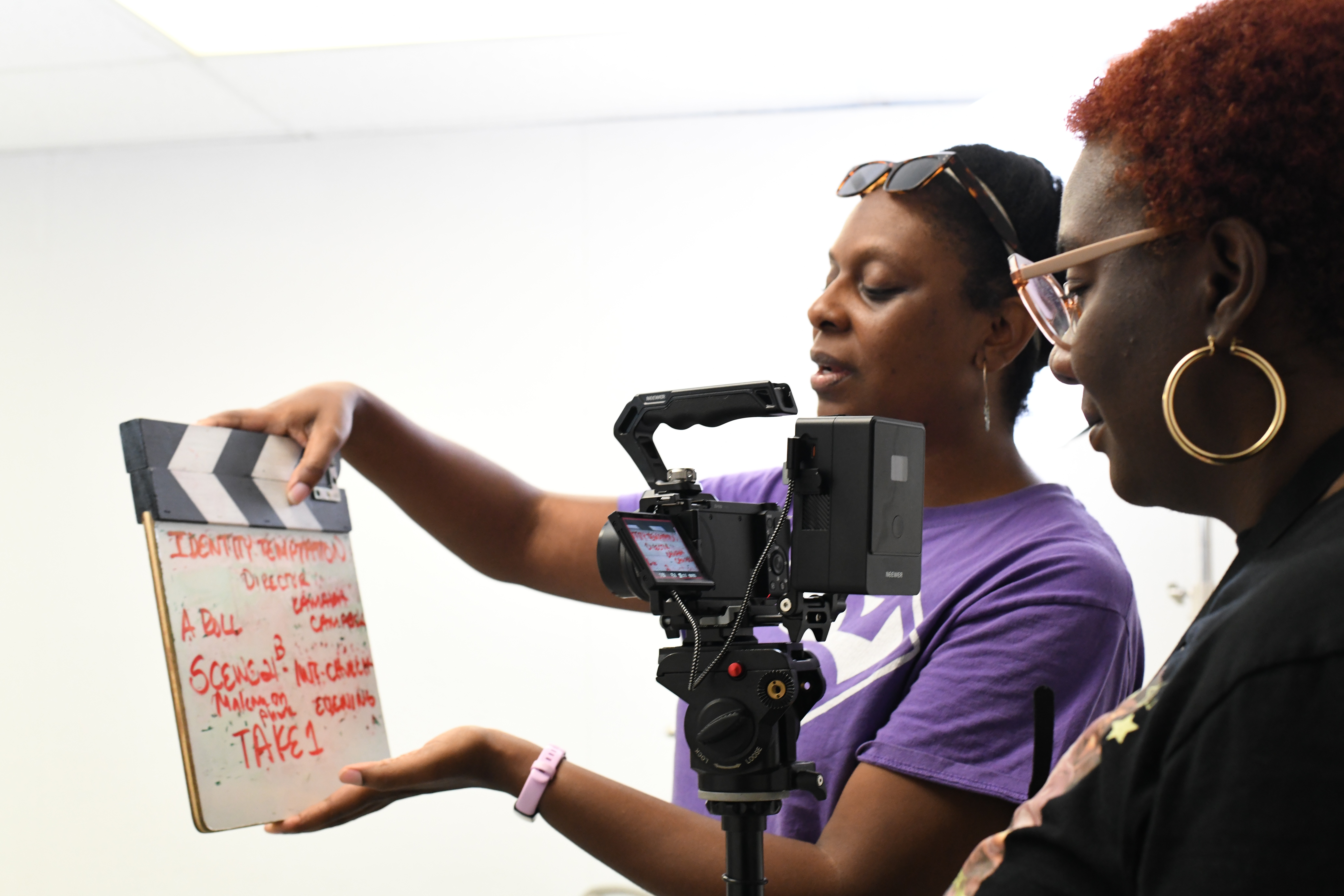 Two women are filming a scene with a camera and a clapperboard, one woman holds the clapperboard, the other operates the camera.