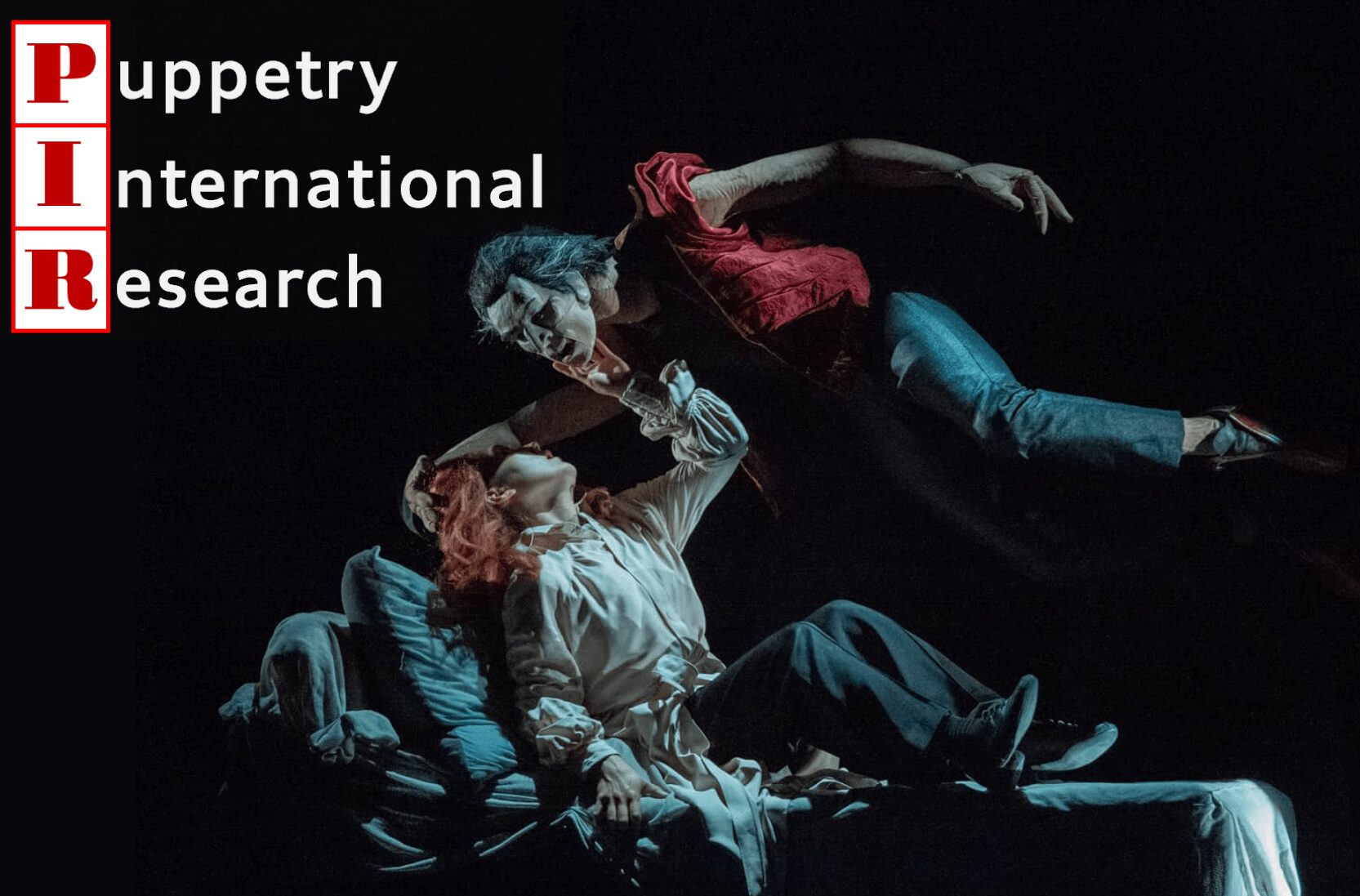 Three performers in dynamic poses on a dark stage, with text reading 'Puppetry International Research' in the top left corner.