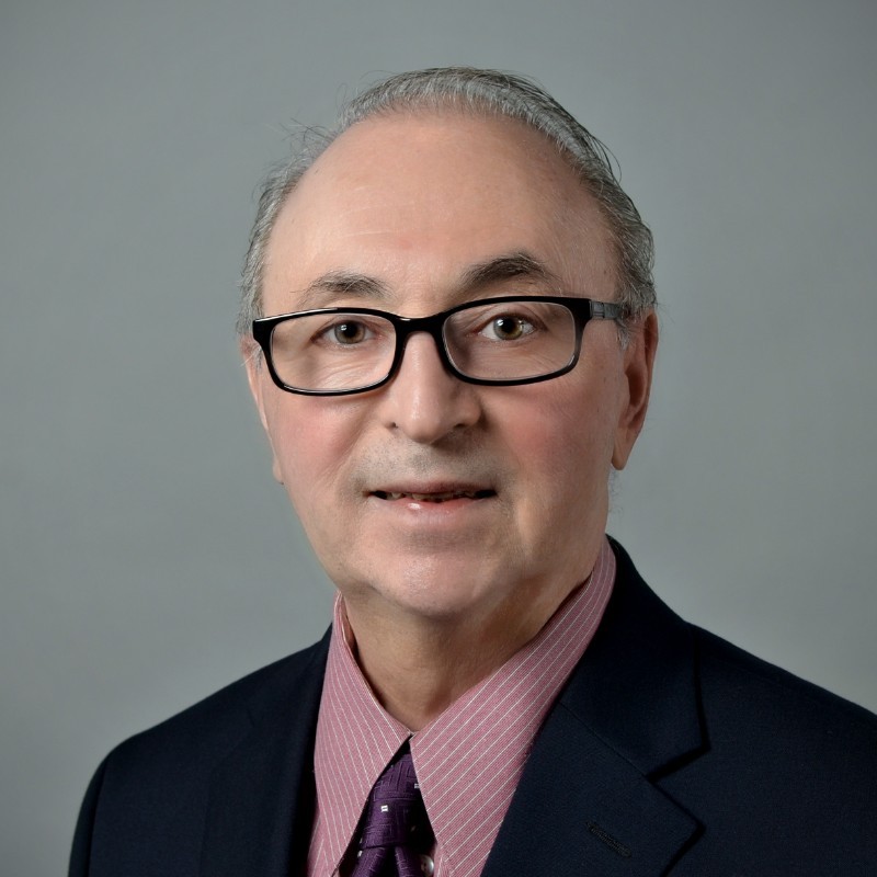 Portrait of a middle-aged man with glasses, wearing a suit and tie, against a plain background.