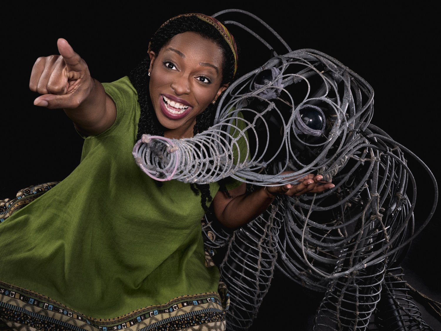 Woman smiling and pointing, holding a wireframe model of an animal, against a black background.