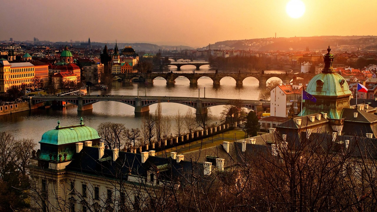 Cityscape with bridges over a river, historic buildings, and a sunset sky.