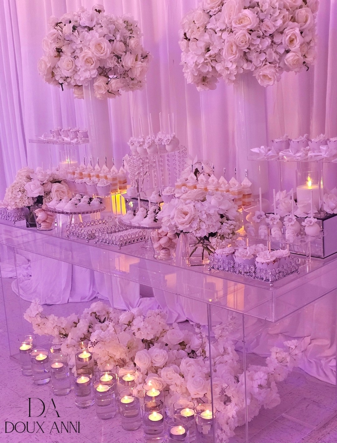 Elegant table with floral arrangements, candles, and glassware, decorated with white flowers and pink lighting, for a celebration or event.