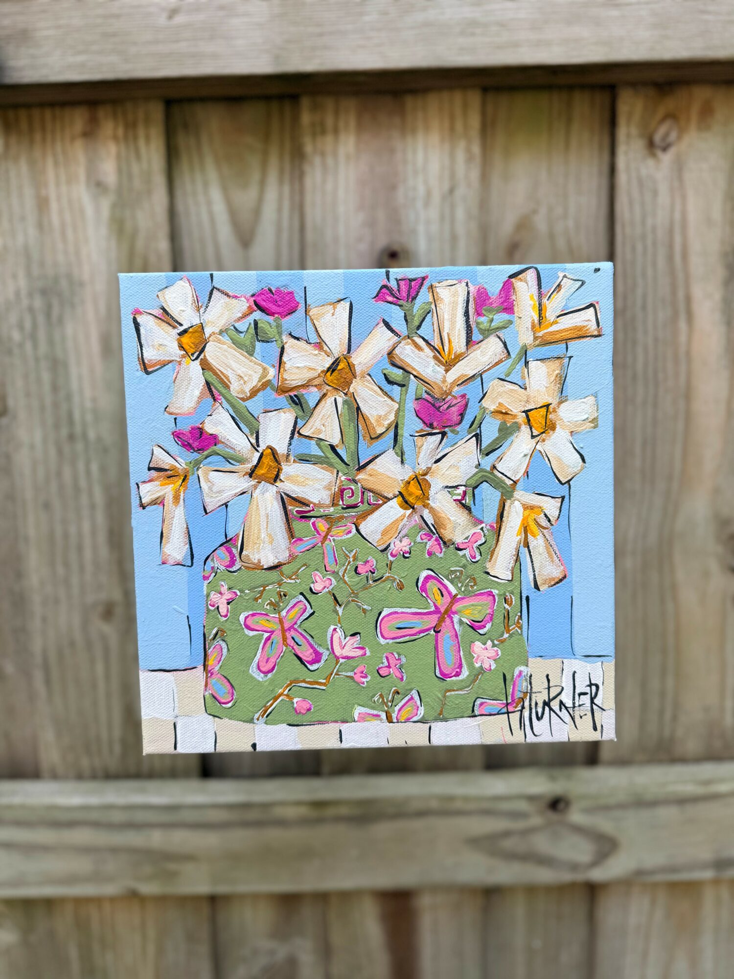 Colorful painting of a green pot with pink bows, white flowers, and purple hearts, against a blue background.