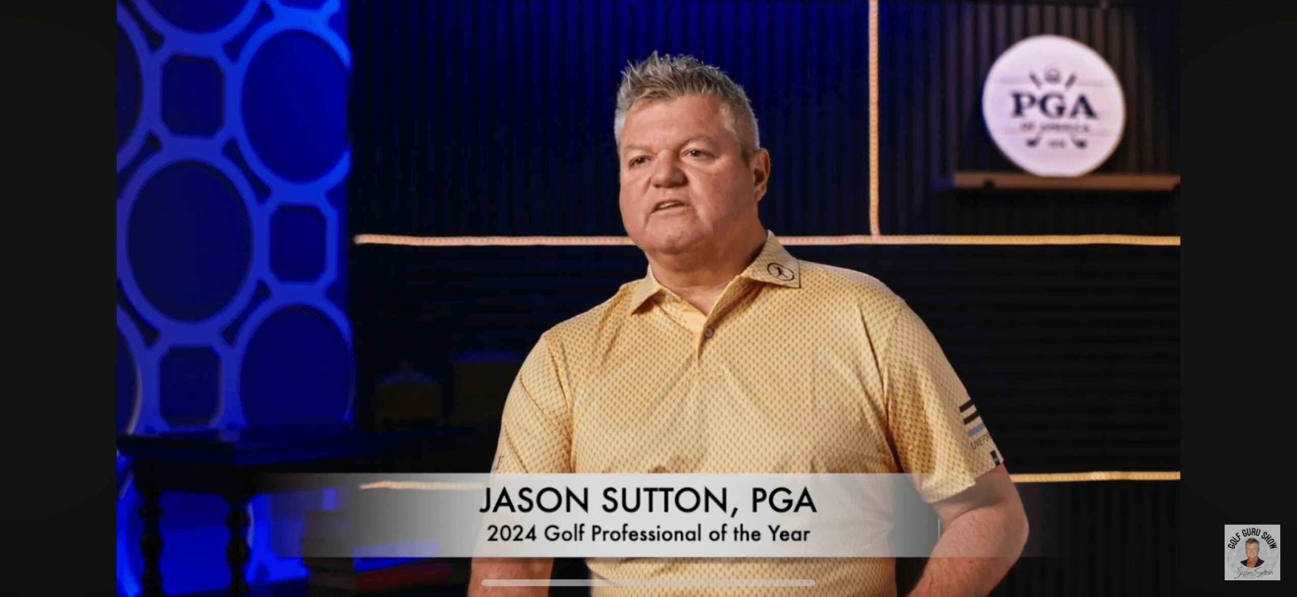 Man in beige polo shirt standing in front of a blue and black background with a PGA logo, during an award presentation.